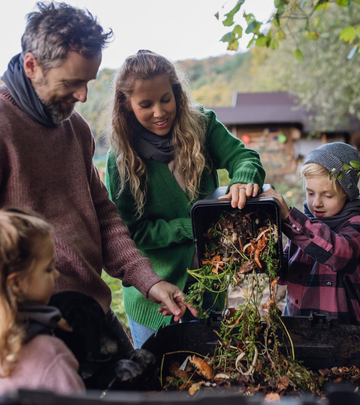 Eine Familie wirft Küchenabfälle auf einen Komposthaufen im Garten.