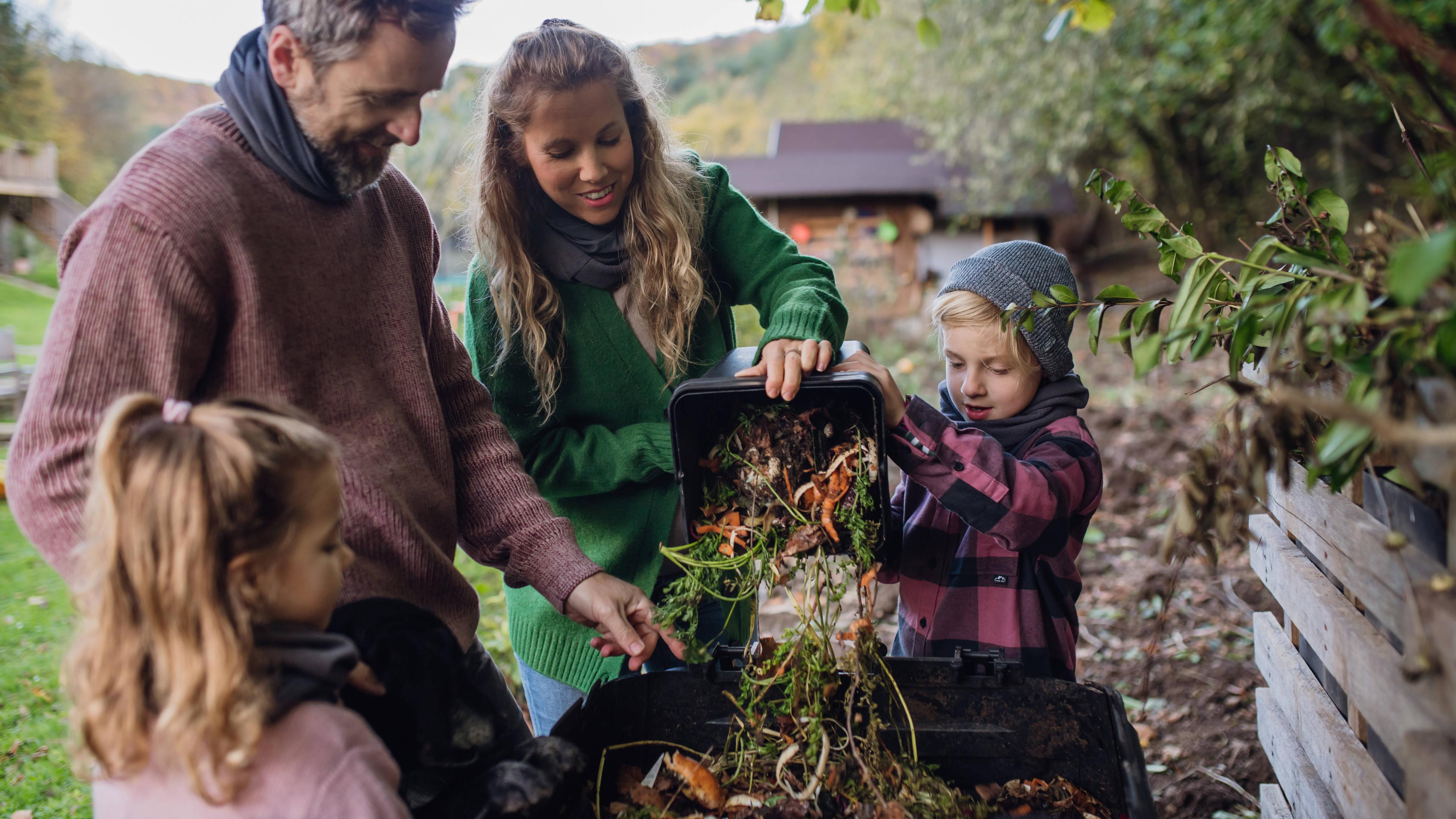 Eine Familie wirft Küchenabfälle auf einen Komposthaufen im Garten.