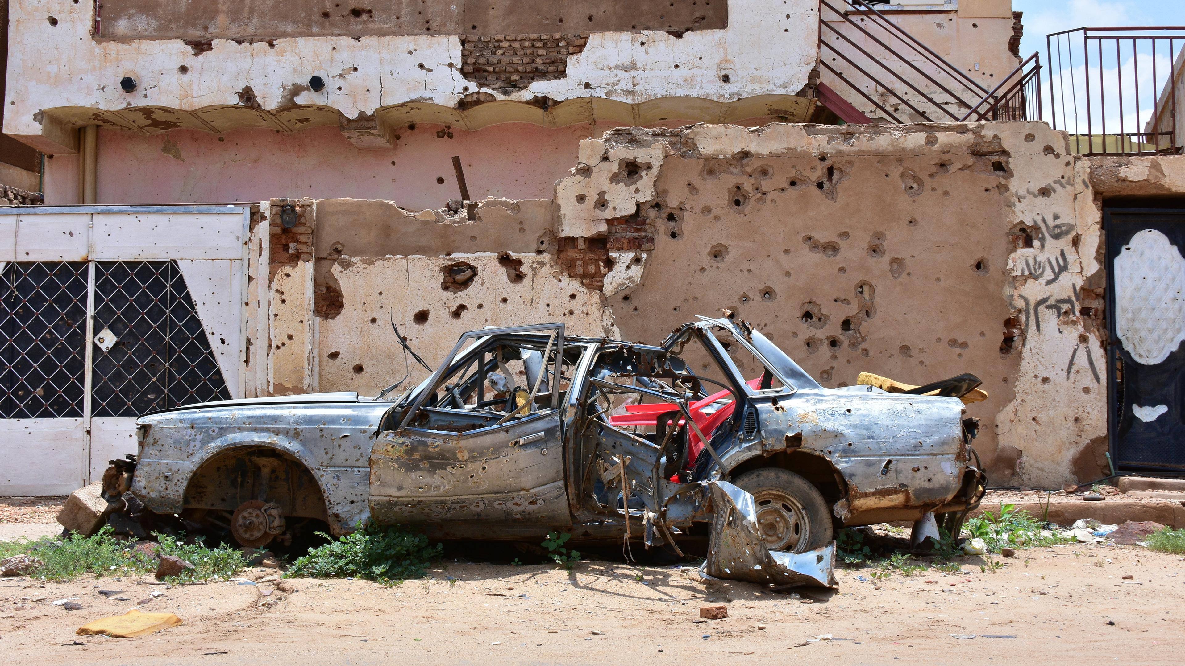 Sudan, Omdurman: Ein zerstörtes Auto steht vor einem Haus voller Einschüsse. Archivbild