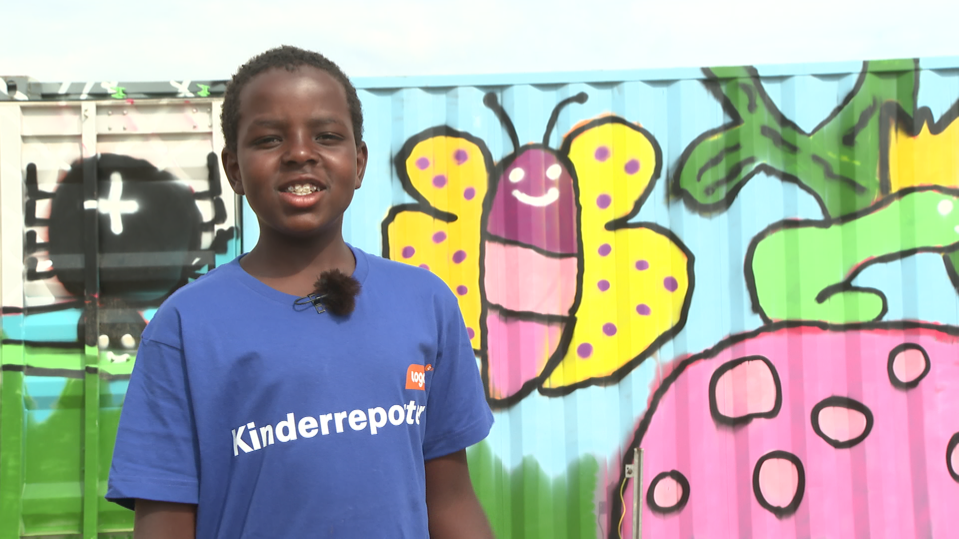 Kinderreporter Momo steht vor bunten Wand