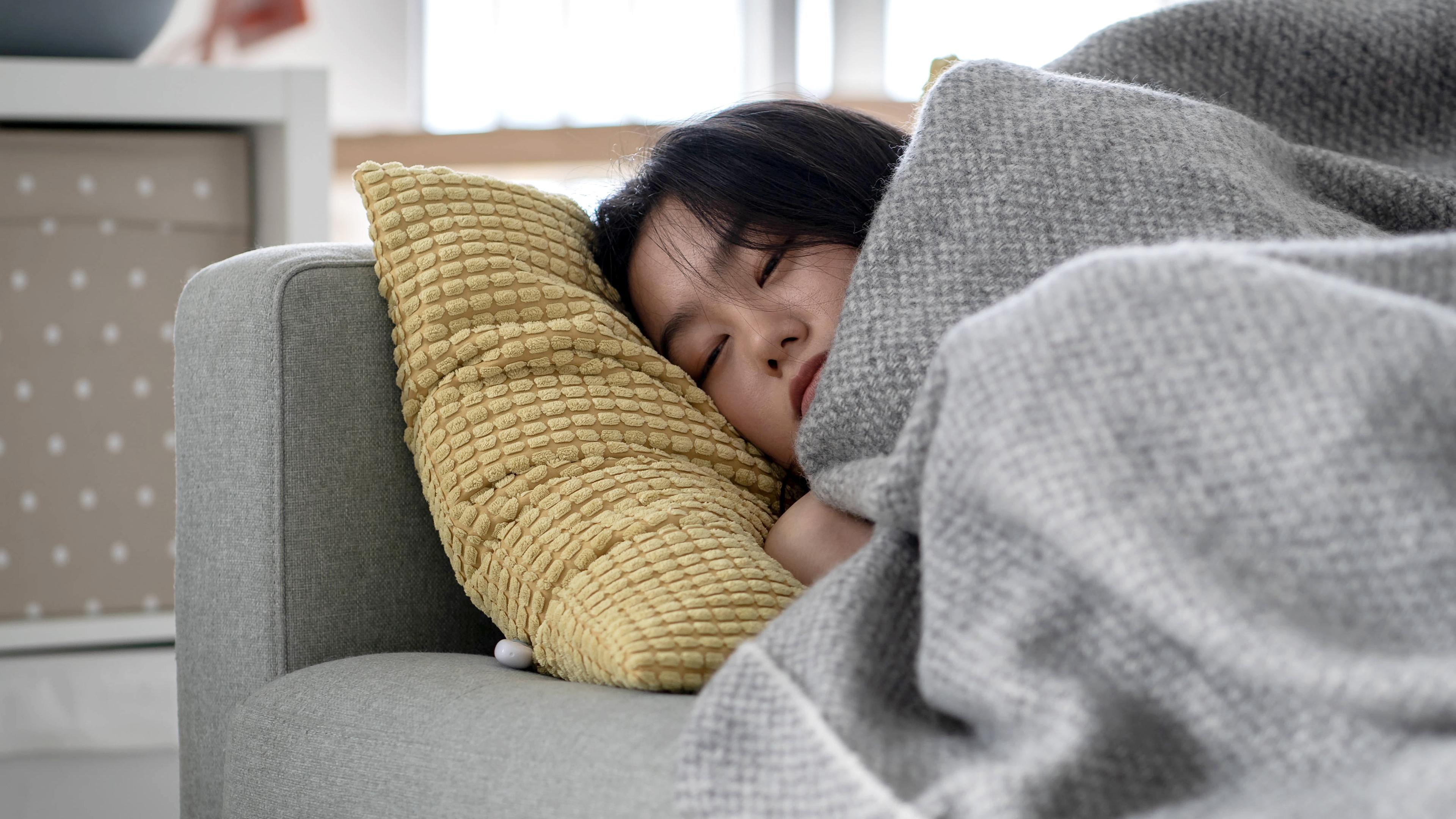 Eine Frau schläft zu Hause auf dem Sofa unter einer Decke und erholt sich von einer Grippe