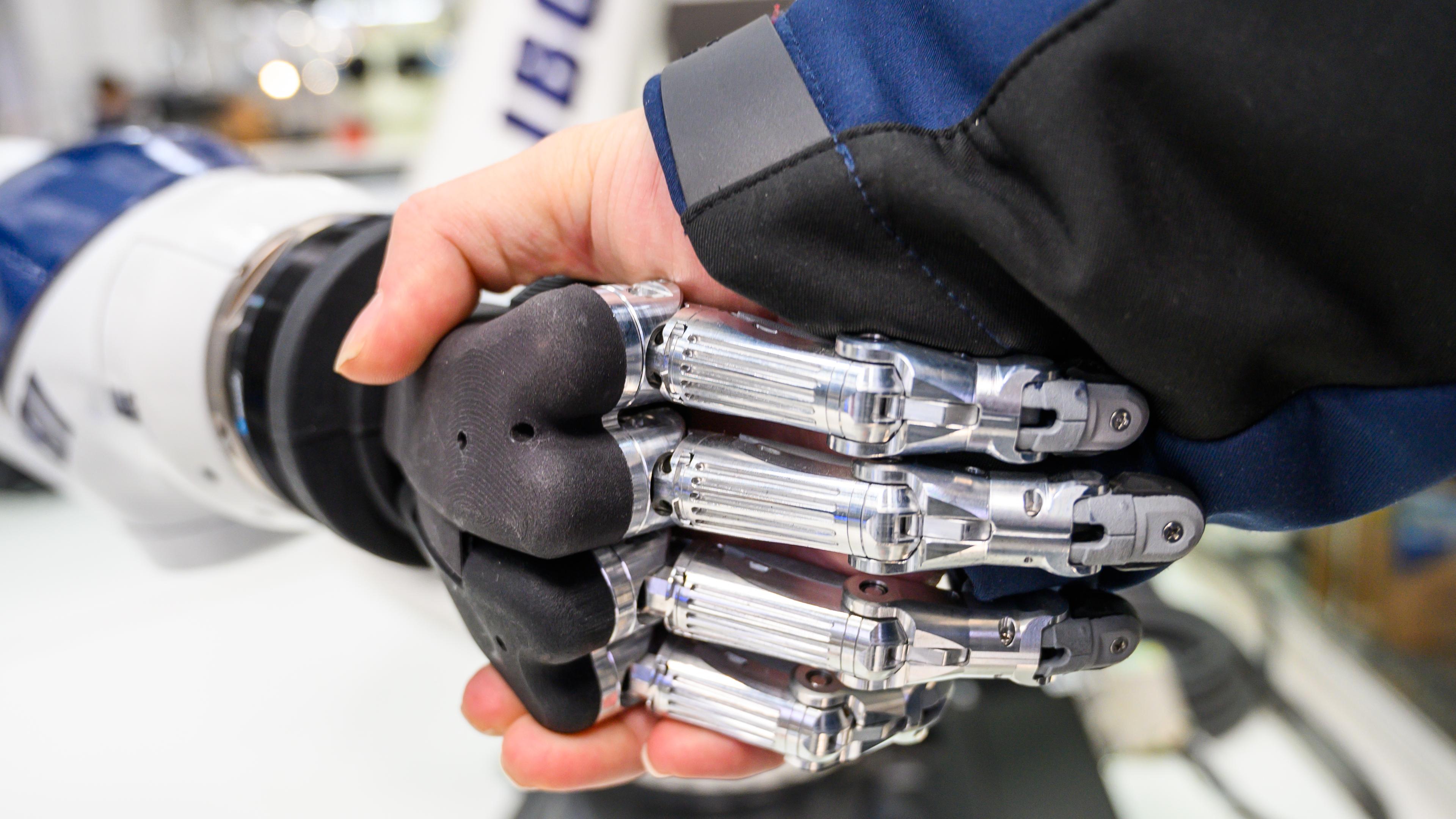 An einem Stand des Herstellers ibg auf der Hannover Messe gibt ein Mann einem Roboter die Hand.