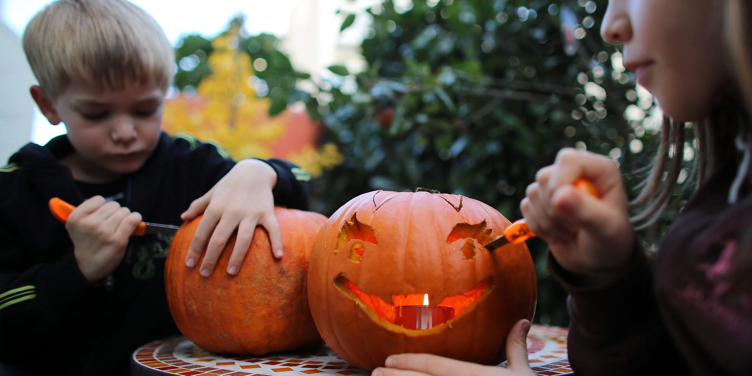 Zwei Kinder schnitzen Kürbisse für Halloween.