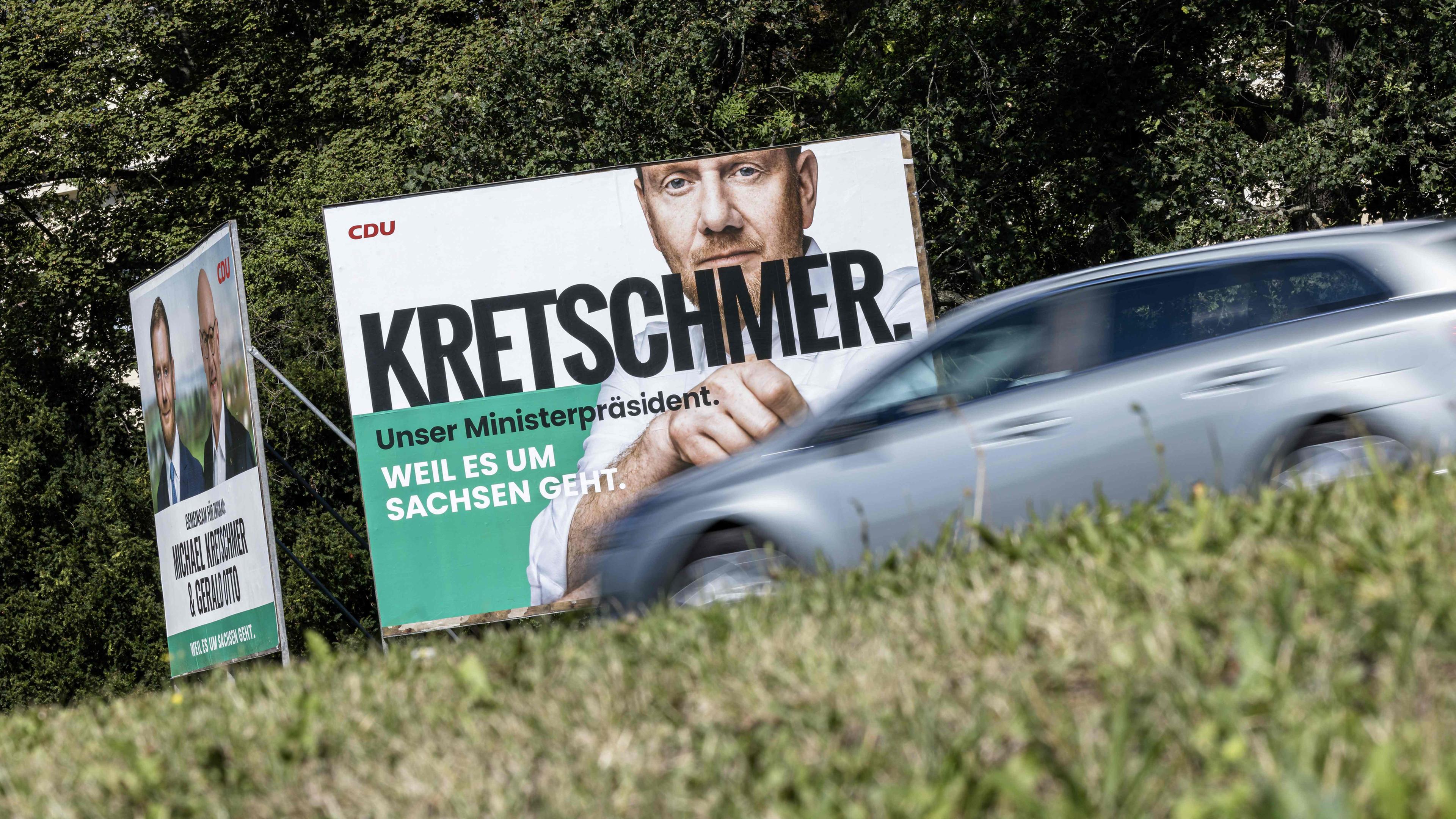 Ein graues Auto fährt an einem großen Wahlkampfplakat von Michael Kretschmer (CDU) vorbei.