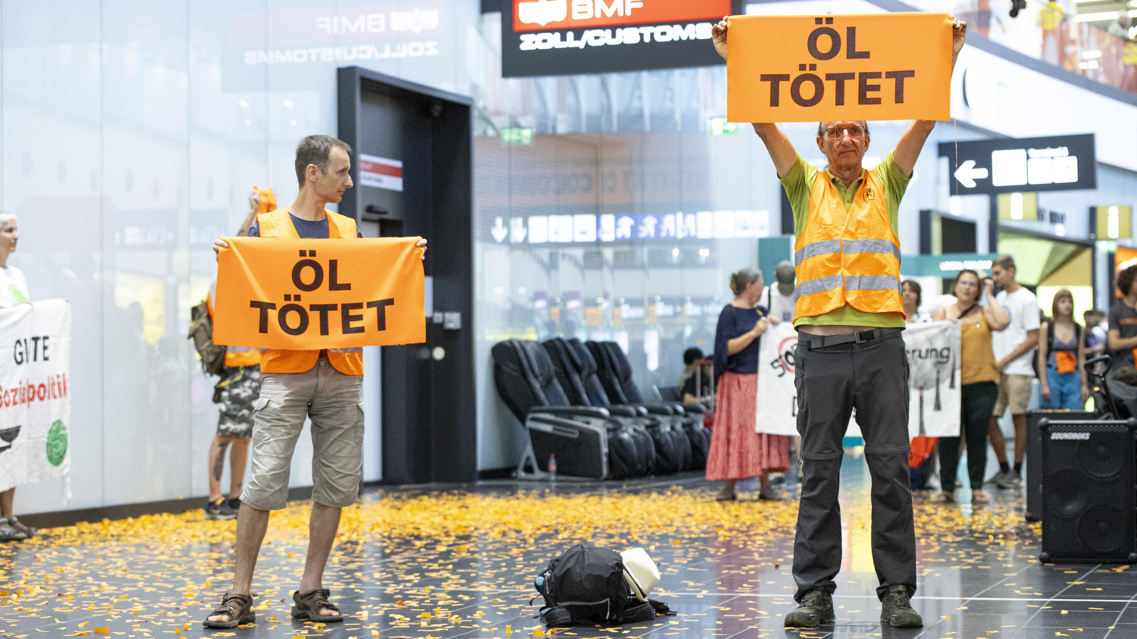 Aktivisten der «Letzten Generation» halten Plakate während einer Störaktion am Flughafen in Wien.