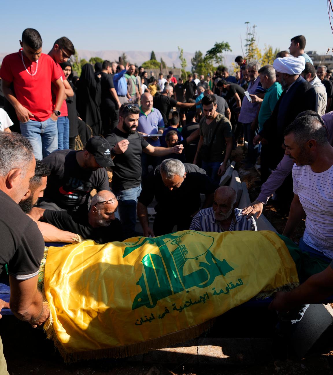 Mourners lower the body of a relative, wrapped in a Hezbollah flag, during the funeral procession in the village of Karak