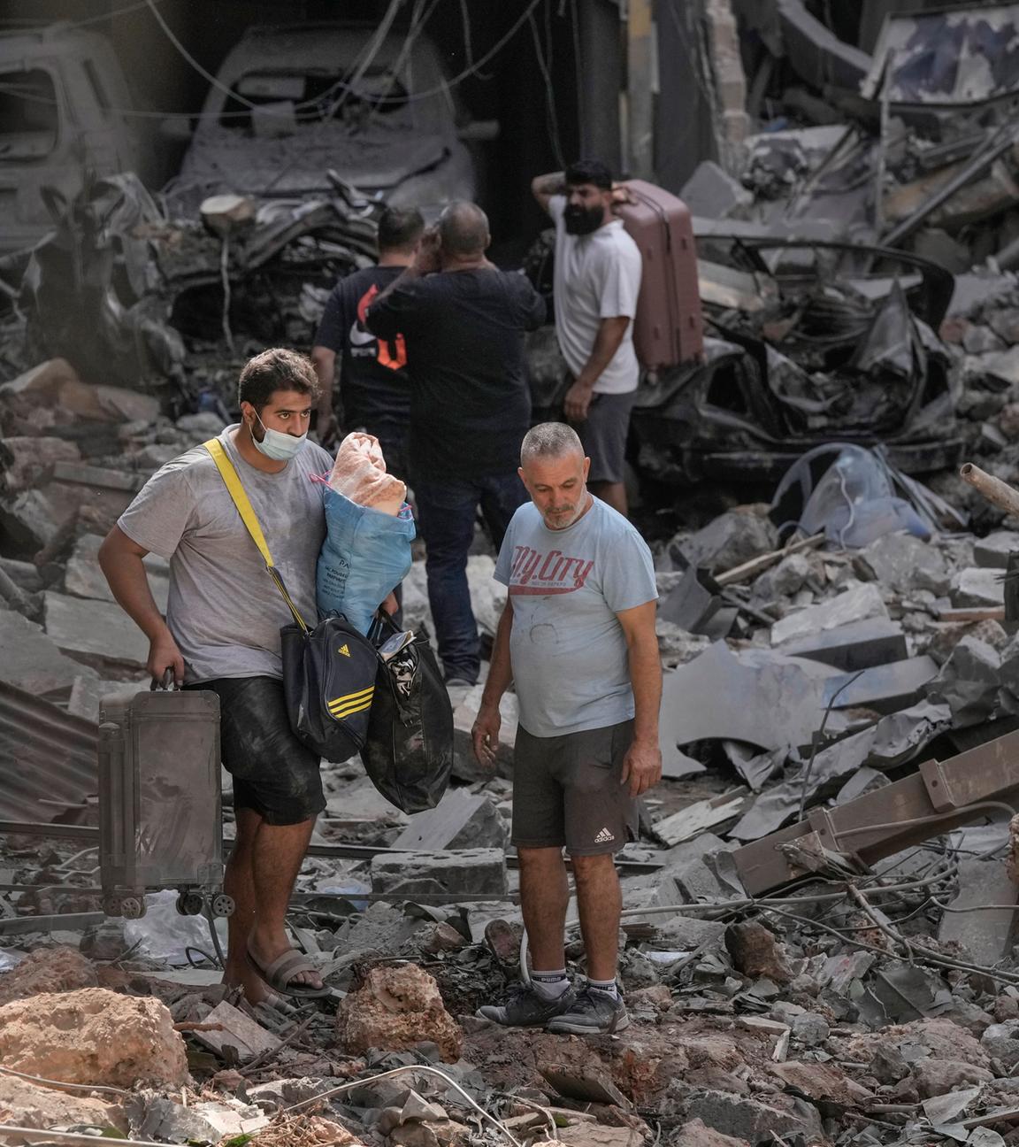 Bewohner gehen mit ihren Habseligkeiten auf den Trümmern zerstörter Gebäude am Ort des israelischen Luftangriffs in Beirut, Libanon