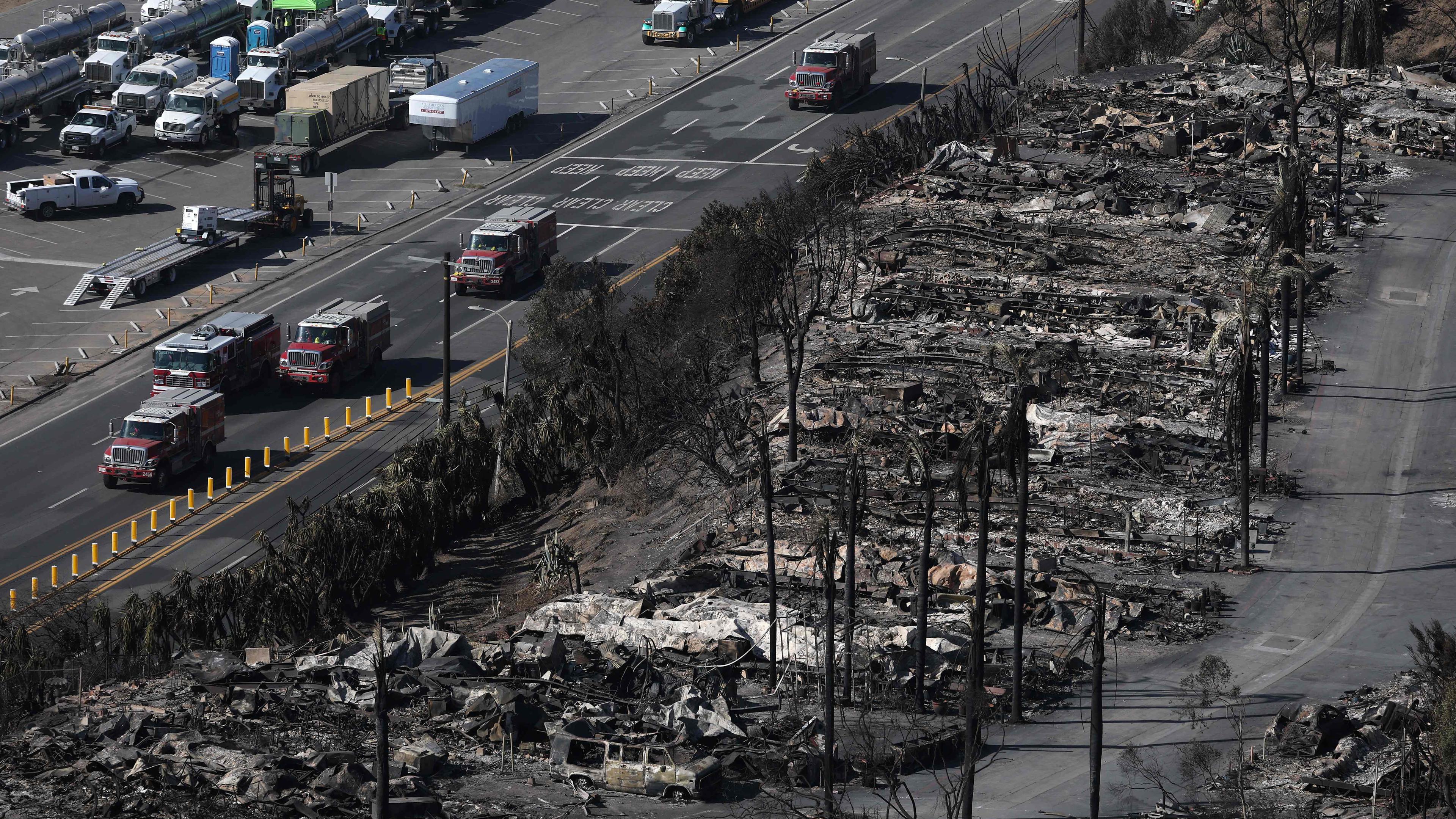 Fahrzeuge der Feuerwehr fahren auf einer Straße neben Brandruinen in der kalifornischen Stadt Los Angeles.