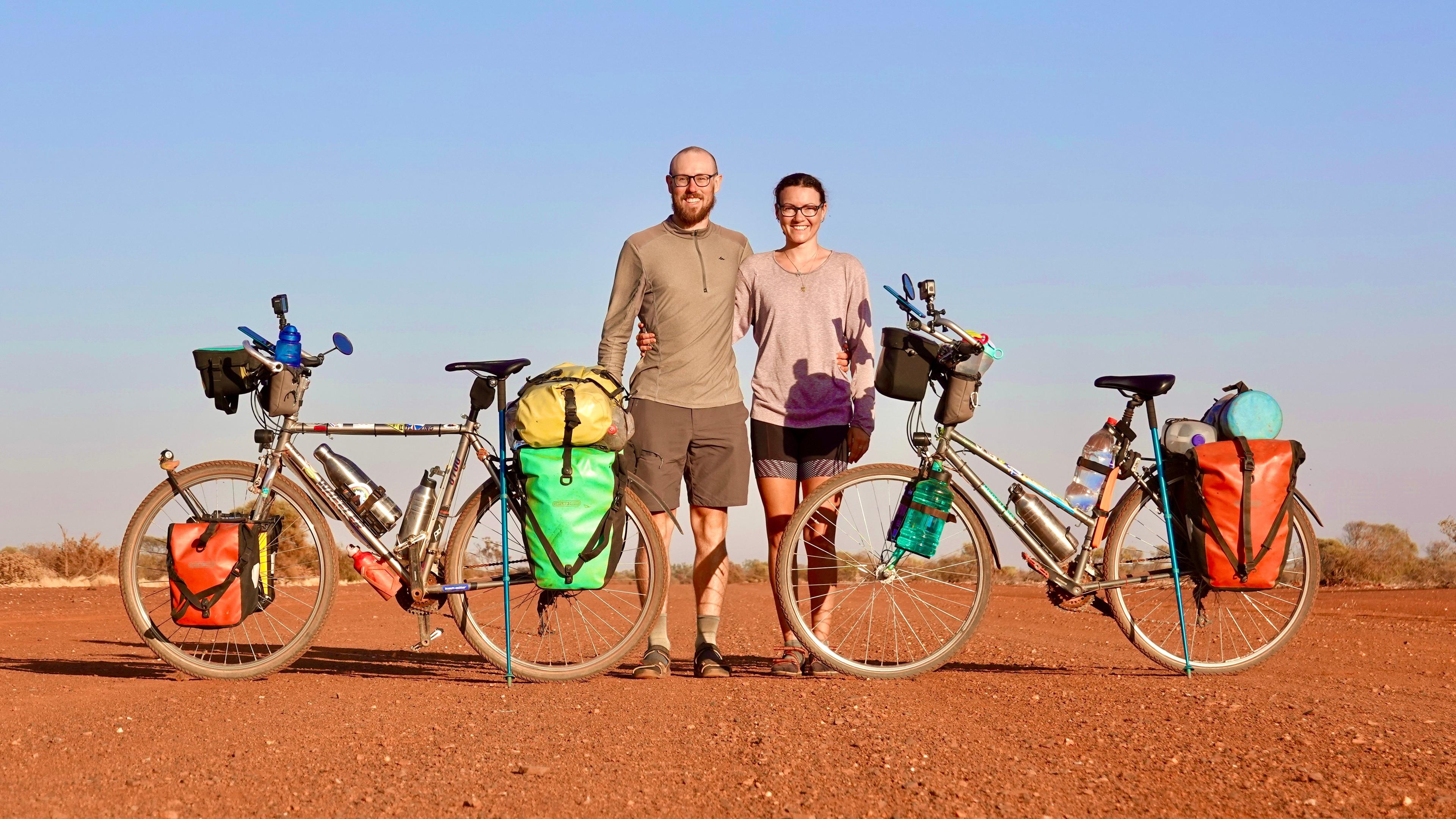 Tobi und Louisa stehen zwischen ihren Fahrrädern in einer kargen Landschaft mit blauem Himmel.