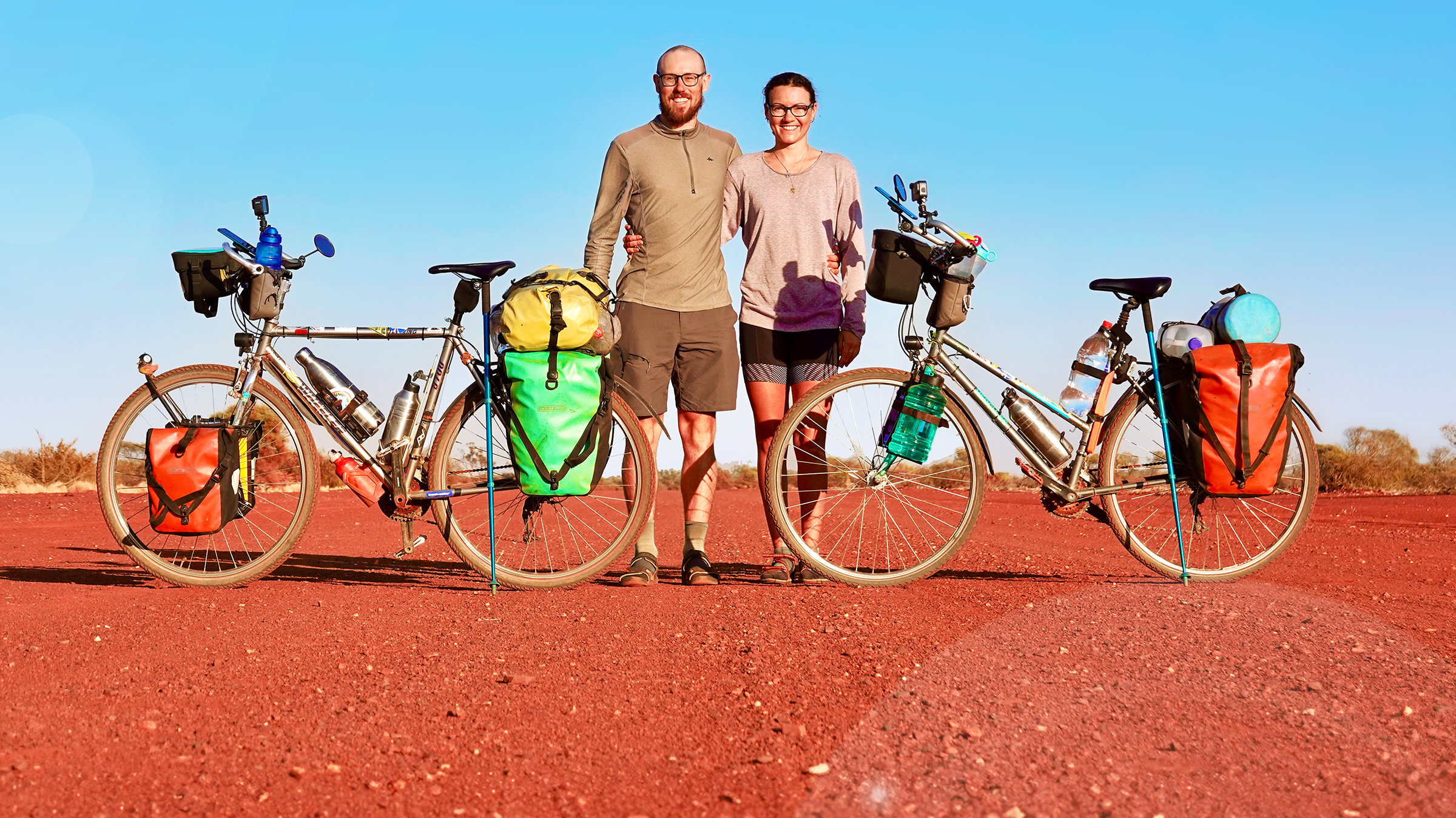 Tobi und Louisa stehen zwischen ihren Fahrrädern in einer kargen Landschaft mit blauem Himmel.