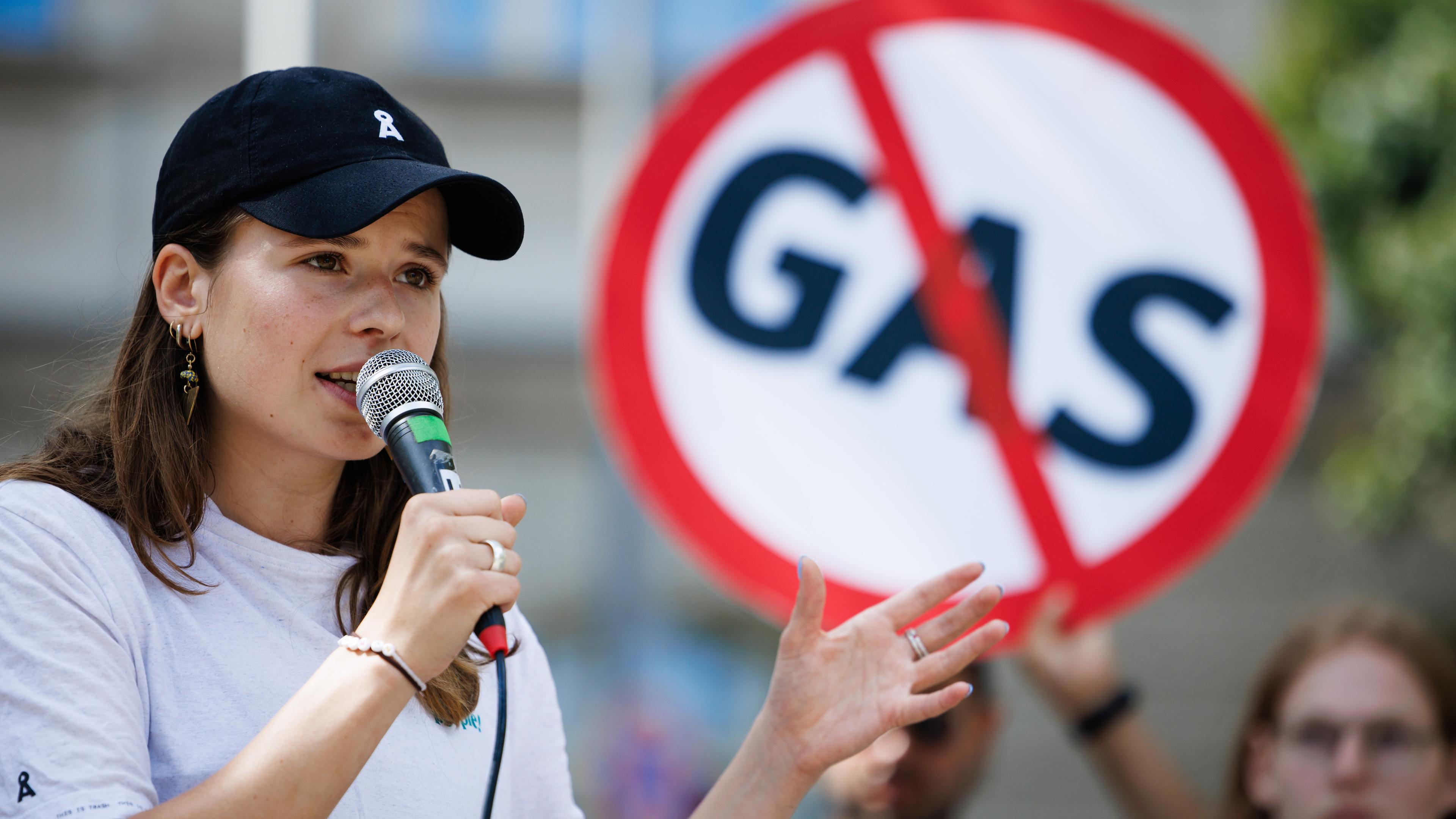 Luisa Neubauer spricht vor einem Schild mit dem durchgestrichenen Wort "Gas".