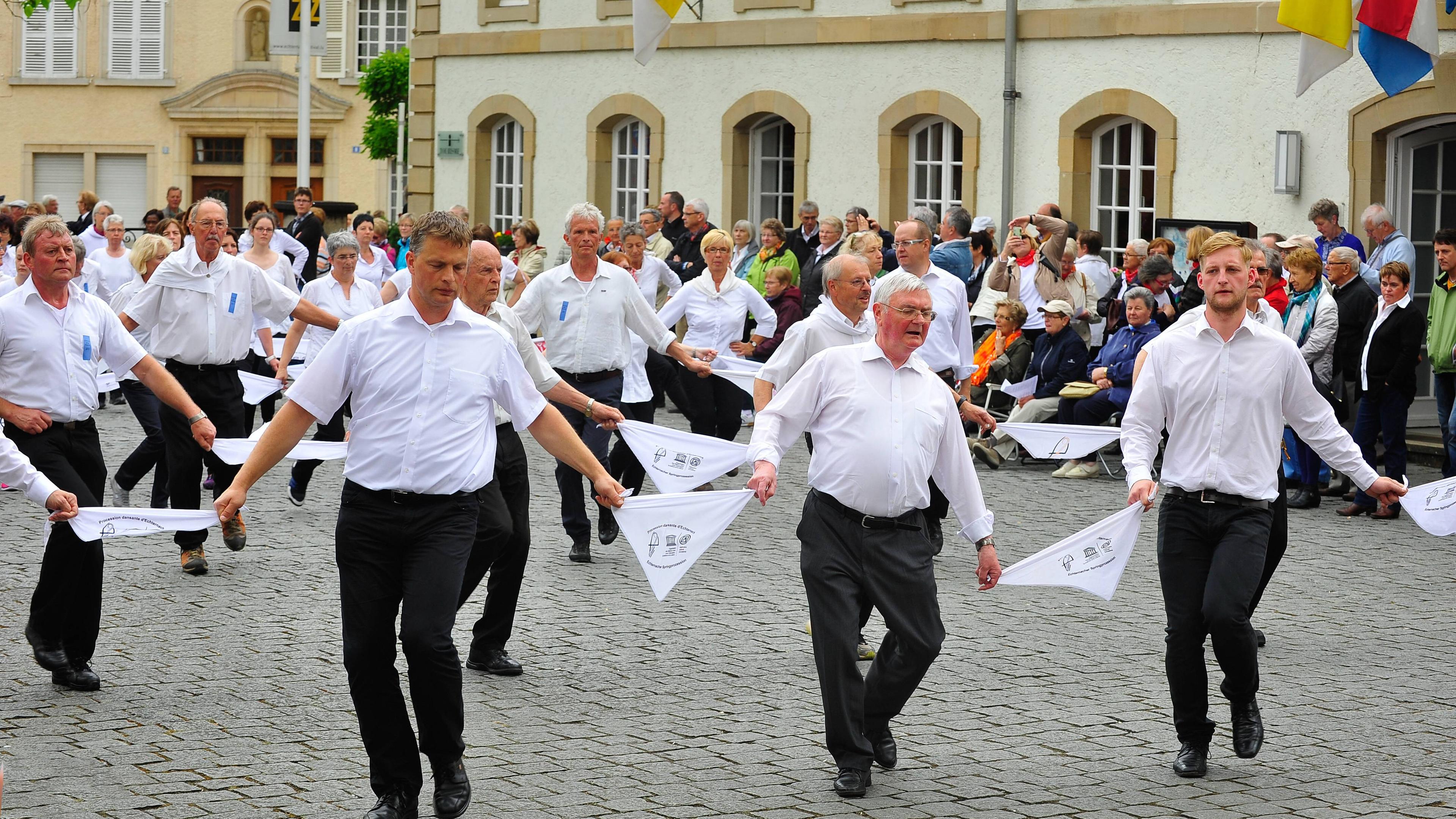 Zu sehen ist die Echternacher Springprozession. Ein Ritual bei dem sich Menschenreihen rhythmisch zu Polka nach vorne bewegen. Die Prozession findet jedes Jahr am Dienstag nach Pfingsten in Echternach, Luxemburg statt.