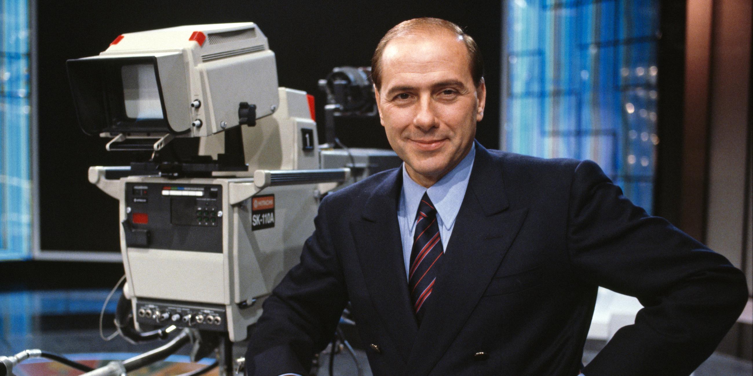 Silvio Berlusconi steht 1986 auf dem Set von Canale 5 in Mailand. Er blickt lächelnd in die Kamera.