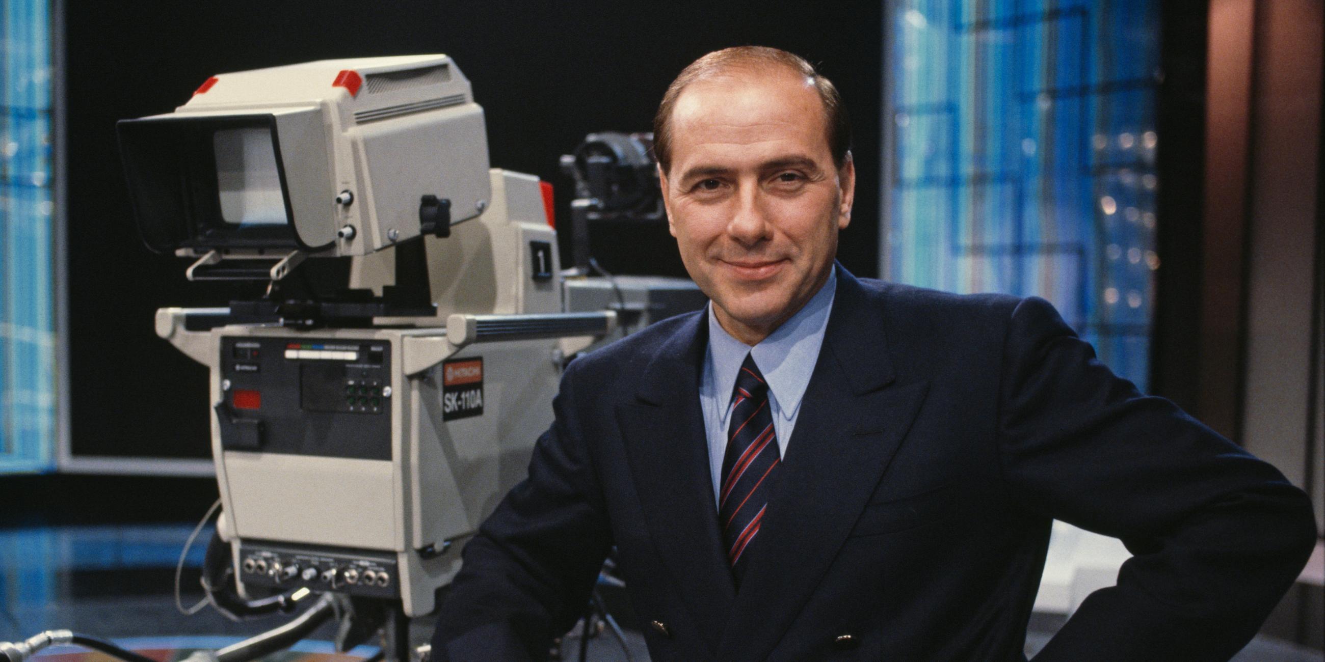 Silvio Berlusconi steht 1986 auf dem Set von Canale 5 in Mailand. Er blickt lächelnd in die Kamera.