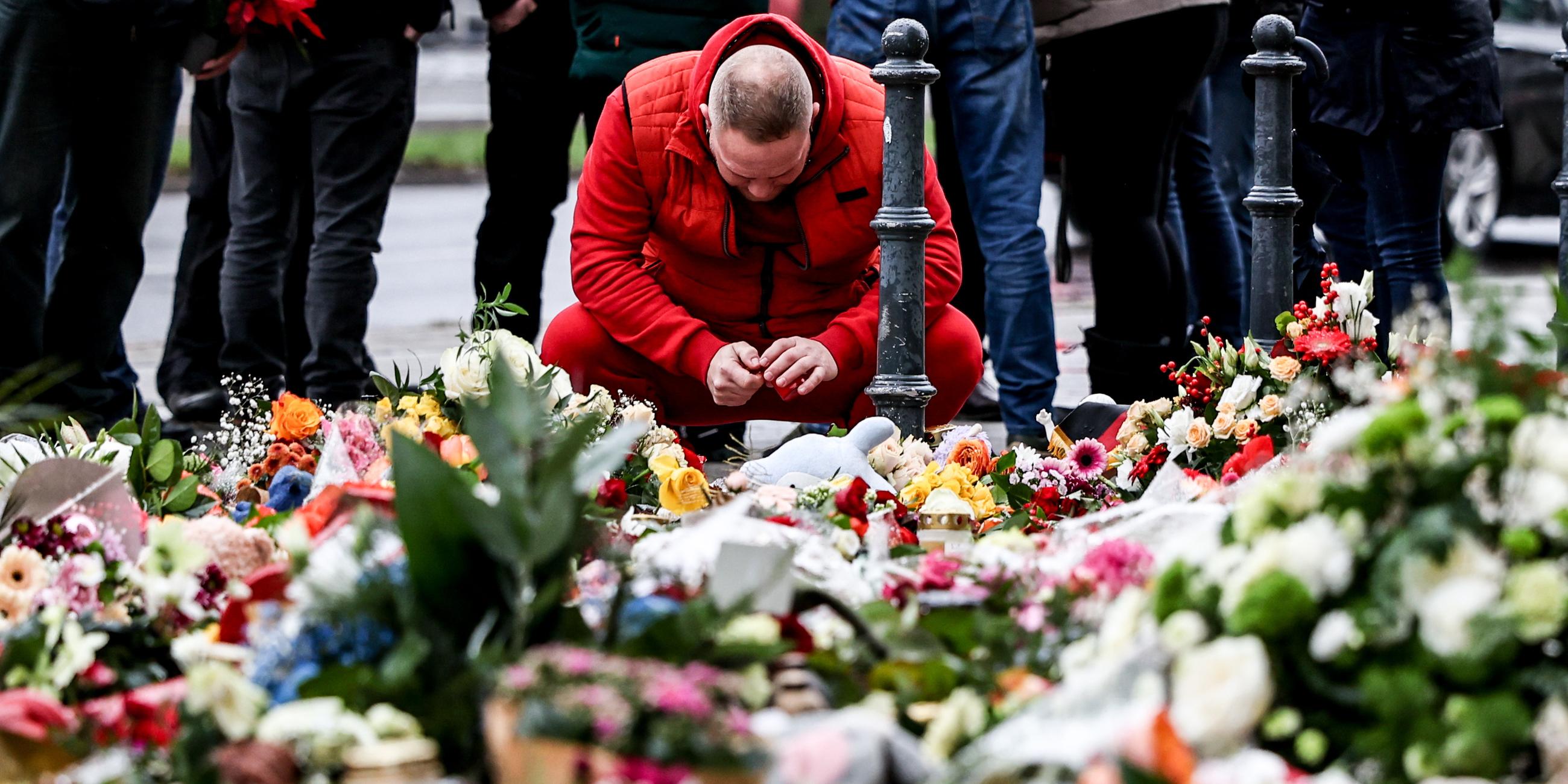 Gedenken an Opfer von Magdeburg: Ein Mann in roter Jacke hockt vor den niedergelegten Blumen 