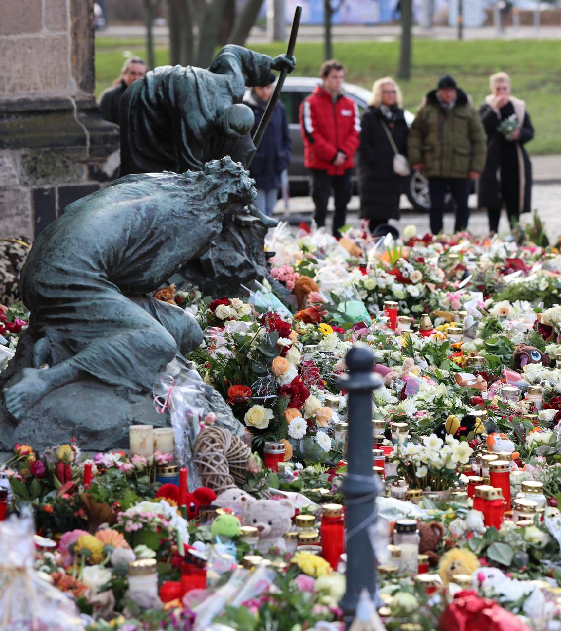 Trauernde stehen vor der Johanniskirche, dem zentralen Gedenkort nach dem Anschlag auf dem Magdeburger Weihnachtsmarkt, vor zahlreichen Kerzen, Blumen und Plüschtieren. 