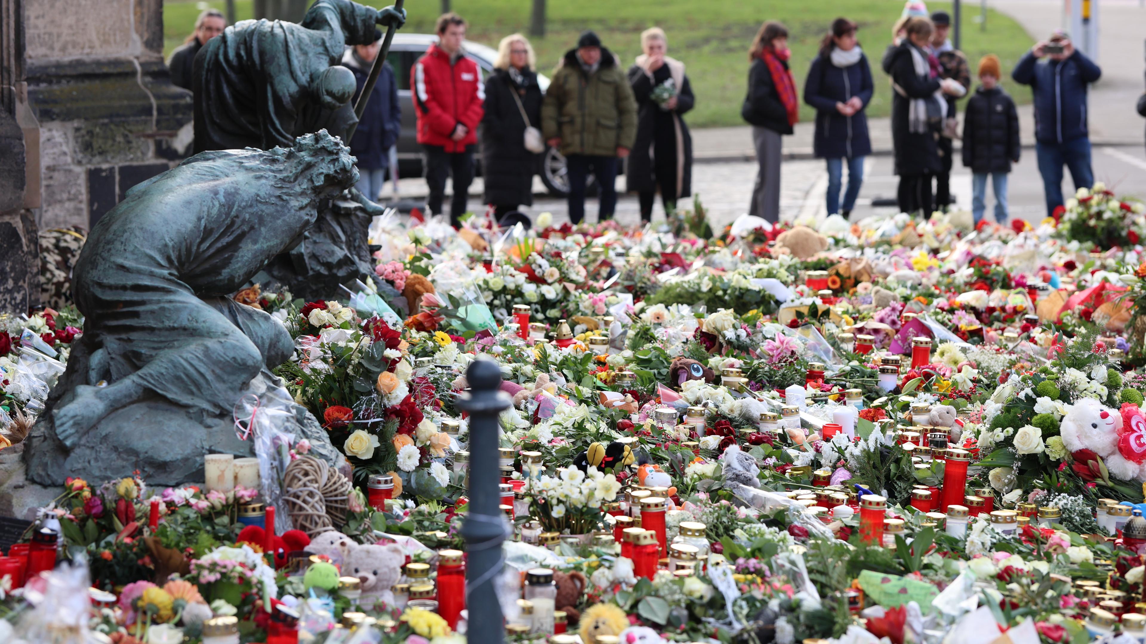 Trauernde stehen vor der Johanniskirche, dem zentralen Gedenkort nach dem Anschlag auf dem Magdeburger Weihnachtsmarkt, vor zahlreichen Kerzen, Blumen und Plüschtieren. 