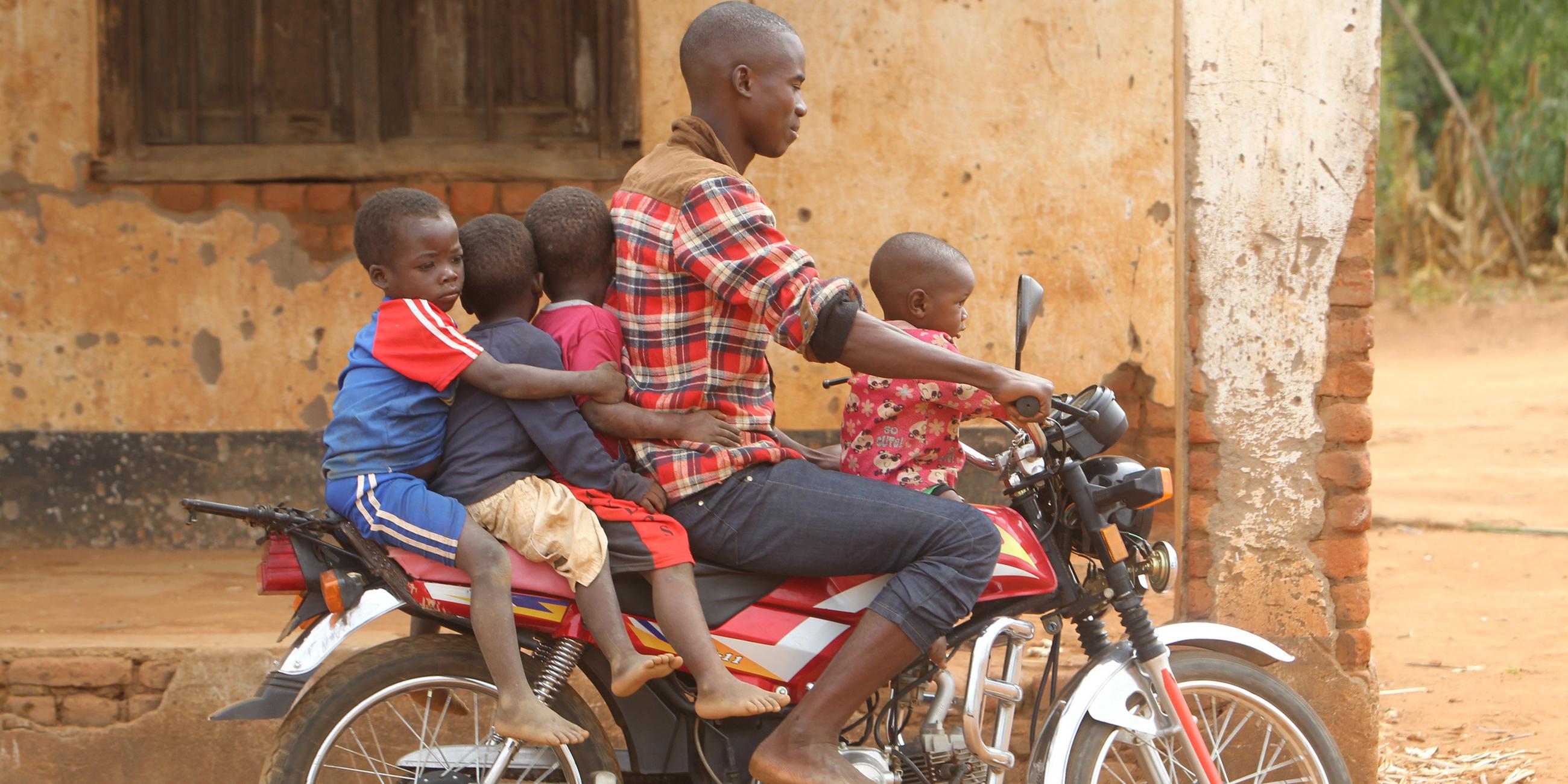 Ein Mann in Malawi transportiert vier Kinder auf einem Motorrad.