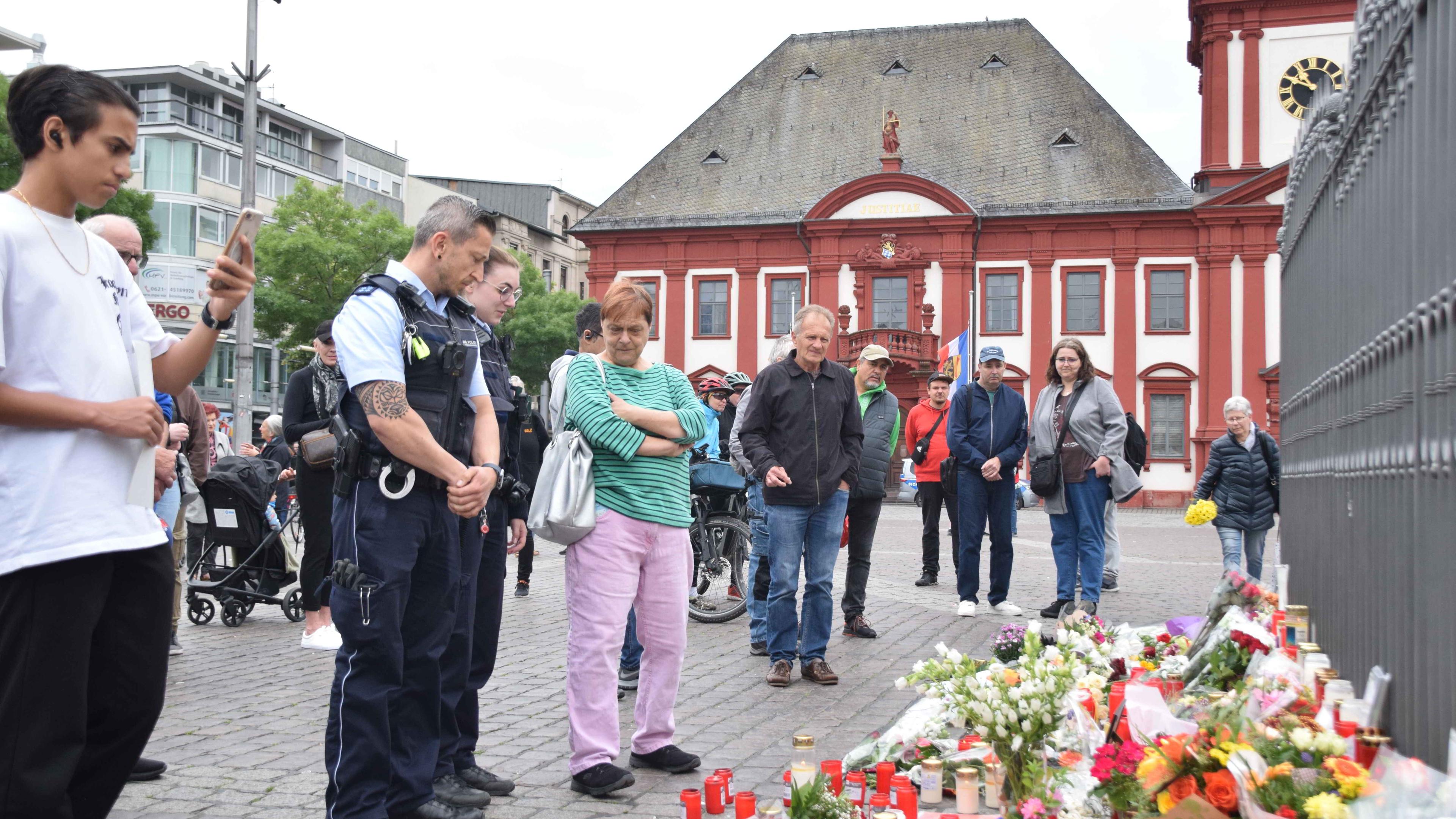Mannheim: Zahlreiche Personen, darunter Polizisten, stehen in unmittelbarer Nähe des Tatorts vor niedergelegten Kerzen und Blumen.