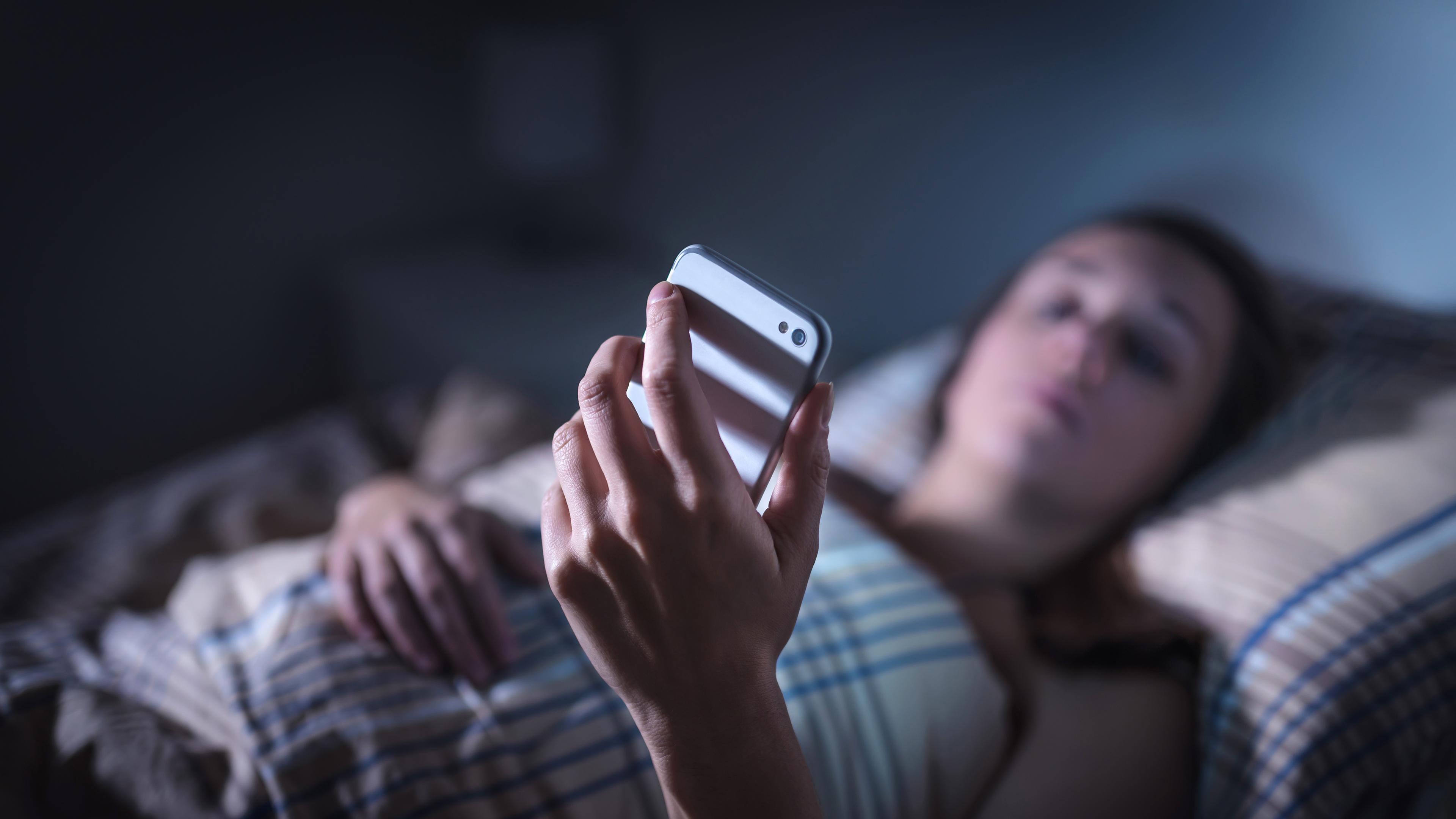 Archiv: Eine Frau schaut im Bett auf ihr Smartphone