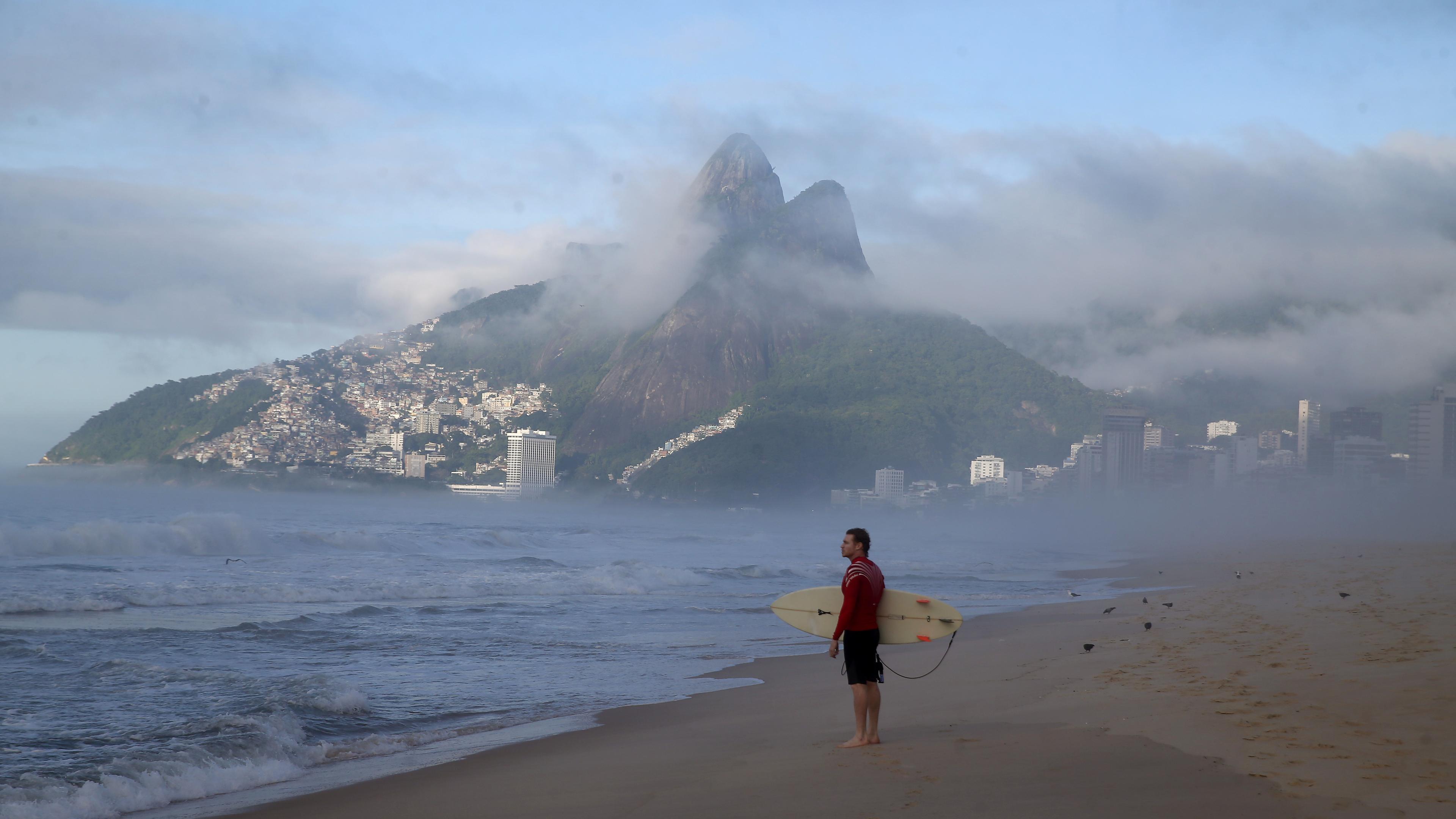 Während die ersten Sonnenstrahlen über die Favela Vidigal fallen, schaut ein Surfer bei Sonnenaufgang am Weihnachtsmorgen am Strand von Ipanema auf die Wellen.