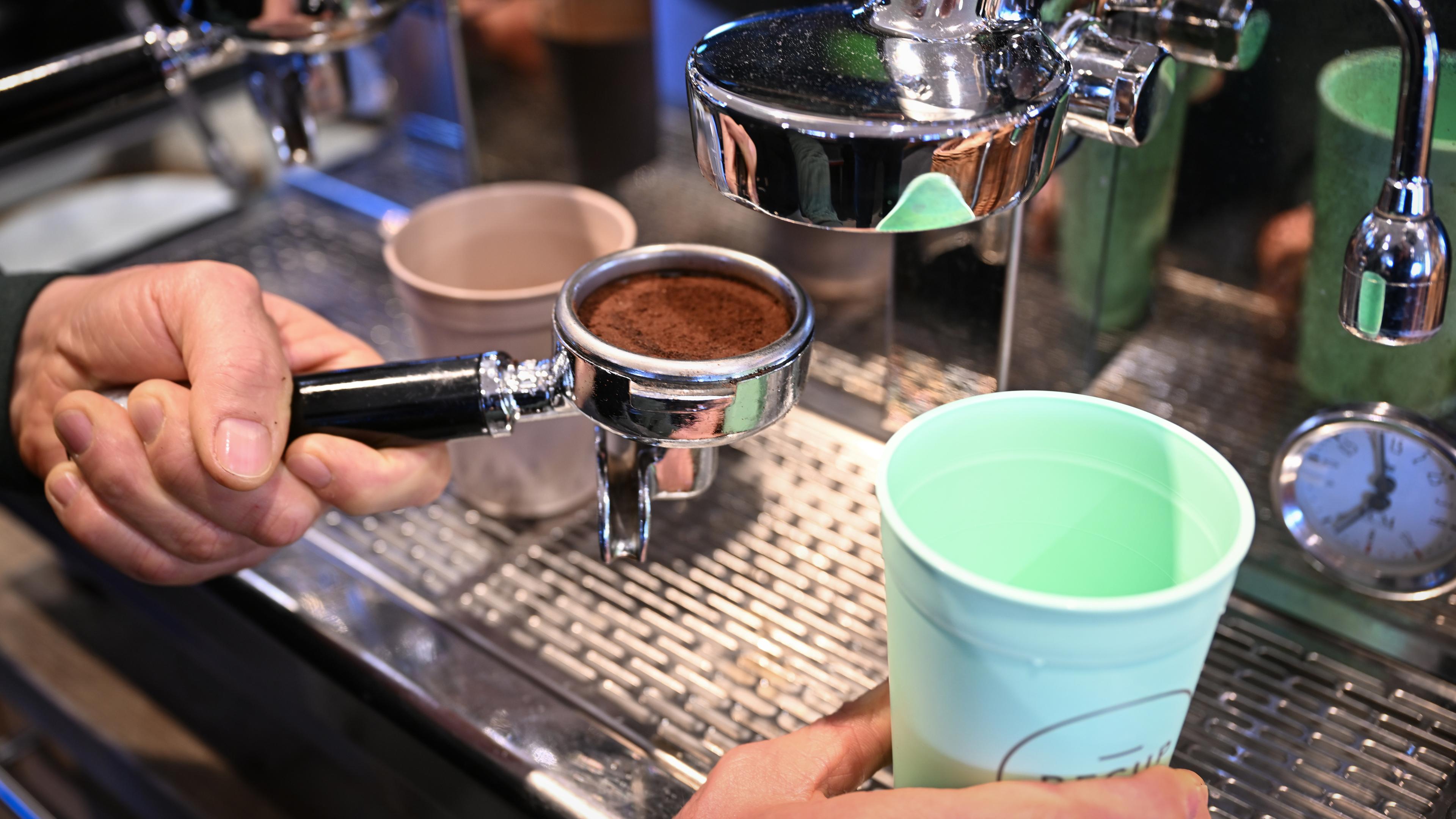 Ein Mitarbeiter eines Bio-Ladens bereitet einen Kaffee in einem Mehrwegbecher zu 