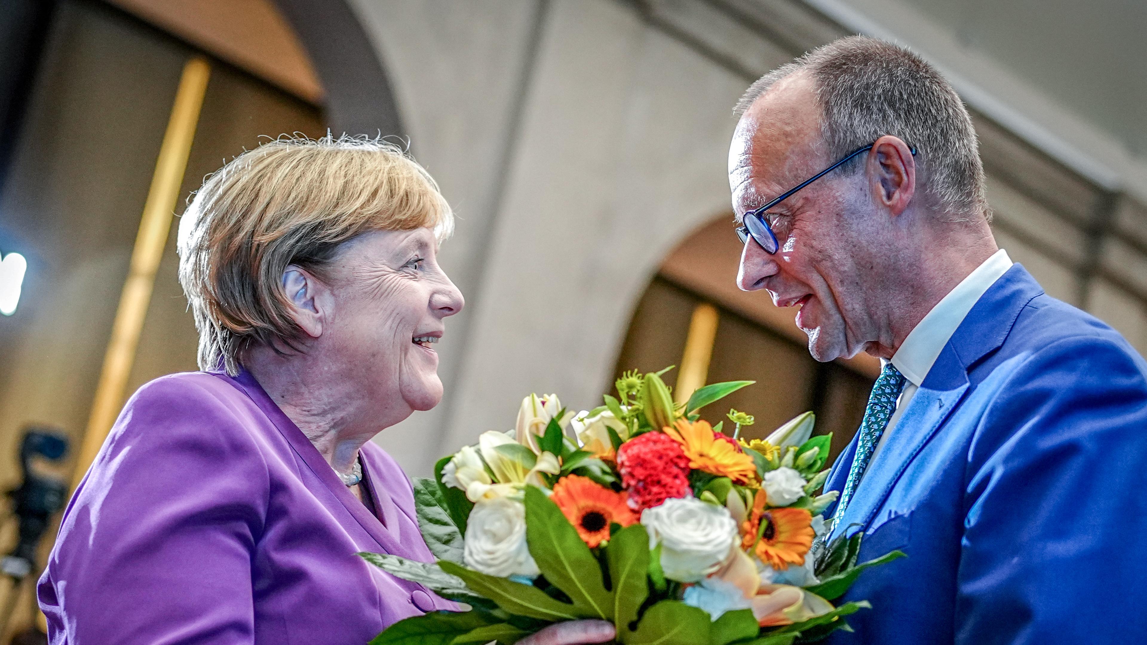 Friedrich Merz übergibt Angela Merkel einen Blumenstrauß.