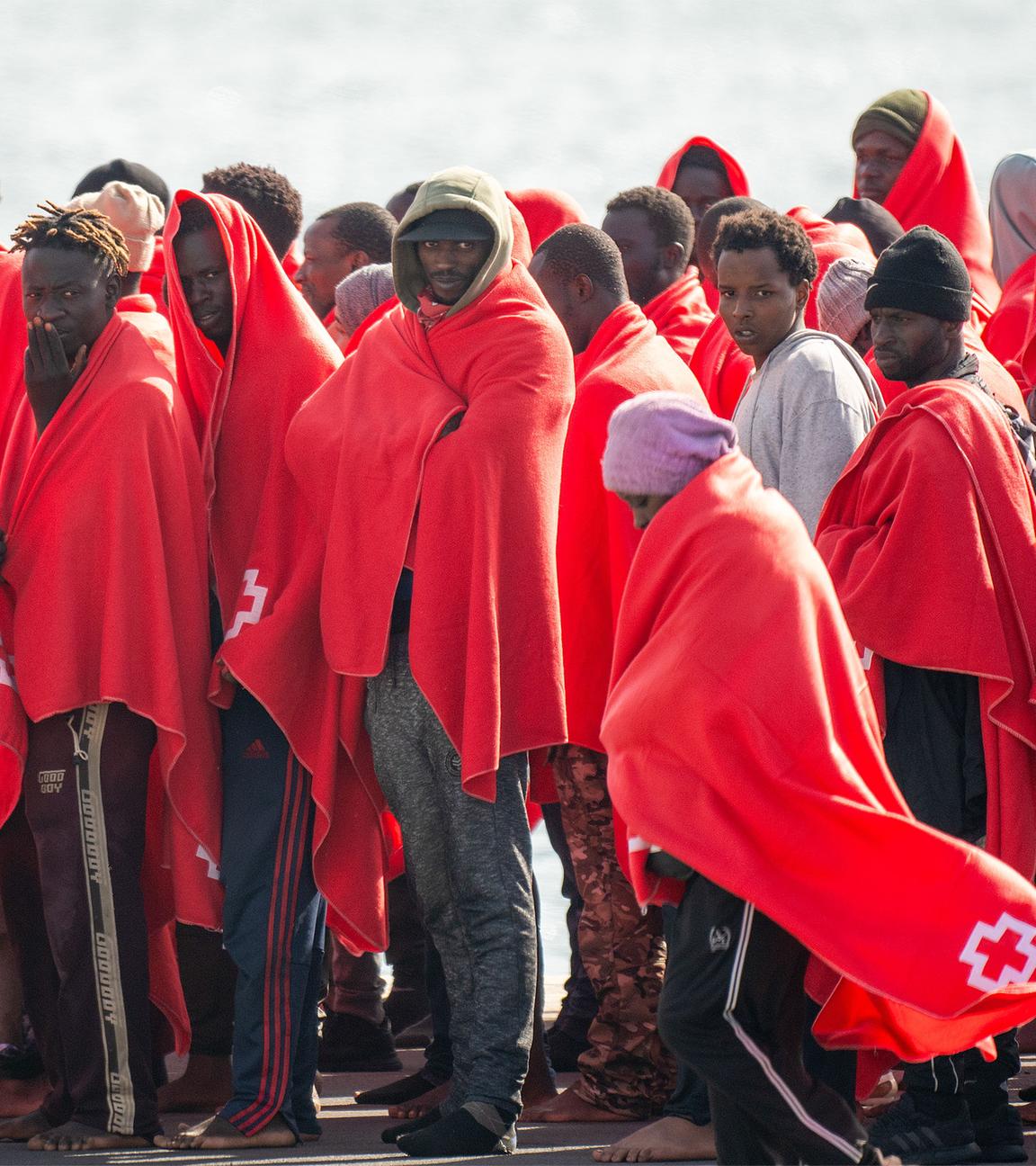 Eine Gruppe von Männern, in rote Decken gehüllt, stehen dicht beisammen