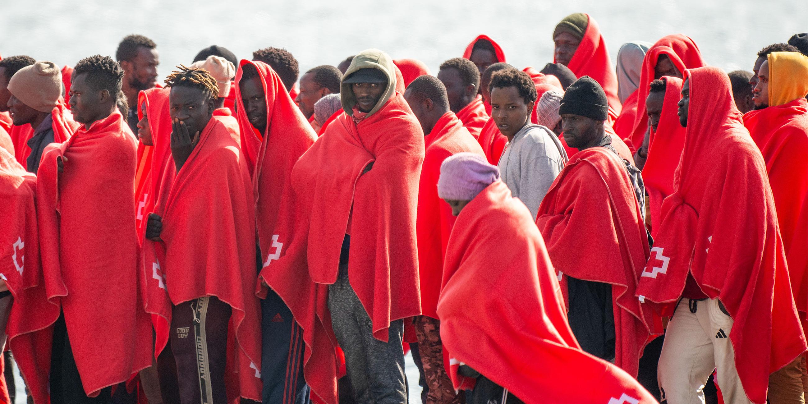 Eine Gruppe von Männern, in rote Decken gehüllt, stehen dicht beisammen