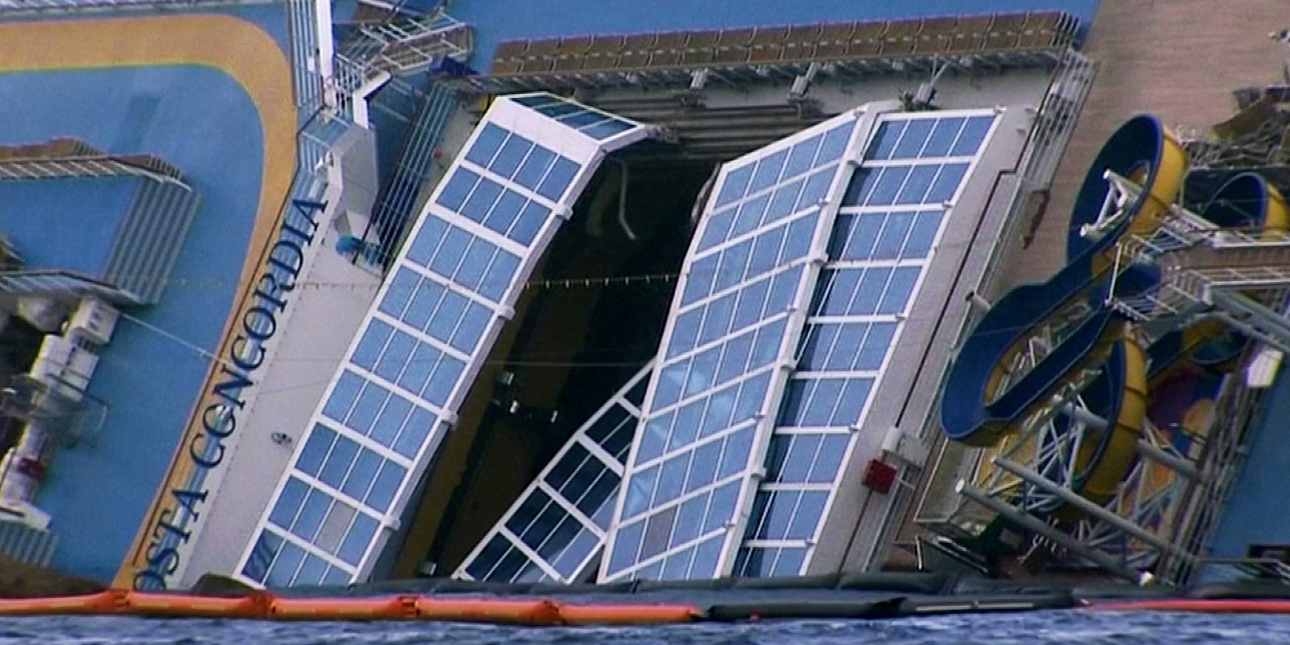 Ein Kreuzfahrtschiff liegt auf der Seite. Auf dem Deck des Schiffes befindet sich eine Wasserrutsche, die fast im 90-Grad-Winkel zum Meeresspiegel liegt.