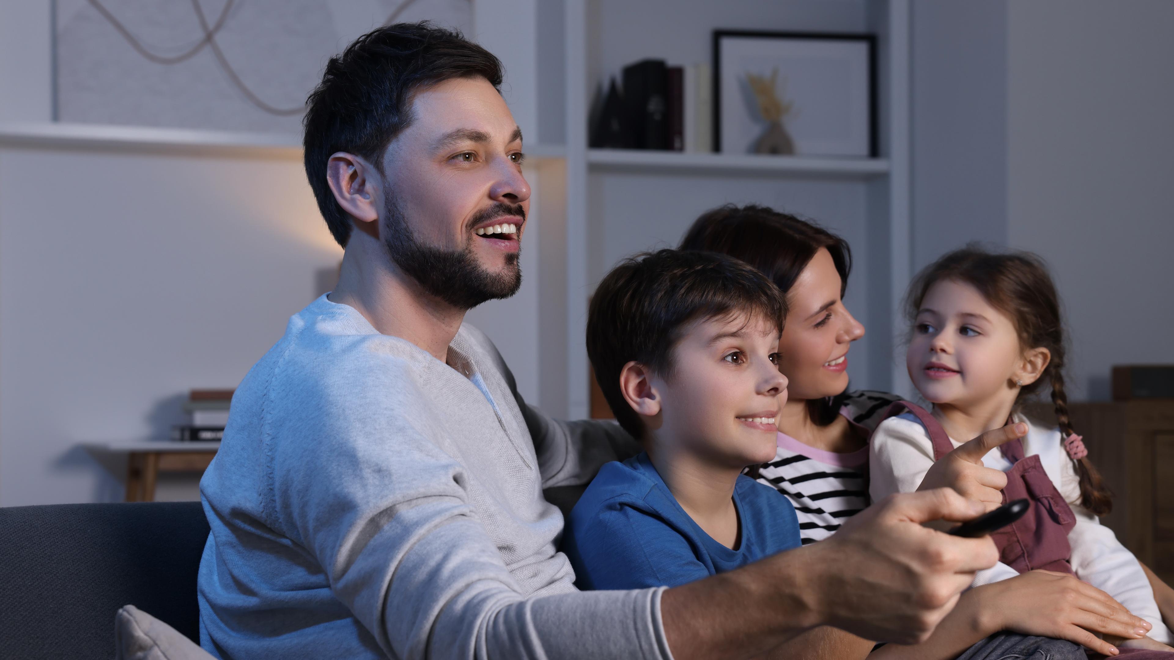 Eltern mit zwei kleinen Kindern auf der Couch beim Fernsehen: Der Vater nutzt die Fernbedienung. Typical für Familie beim Fernsehen.