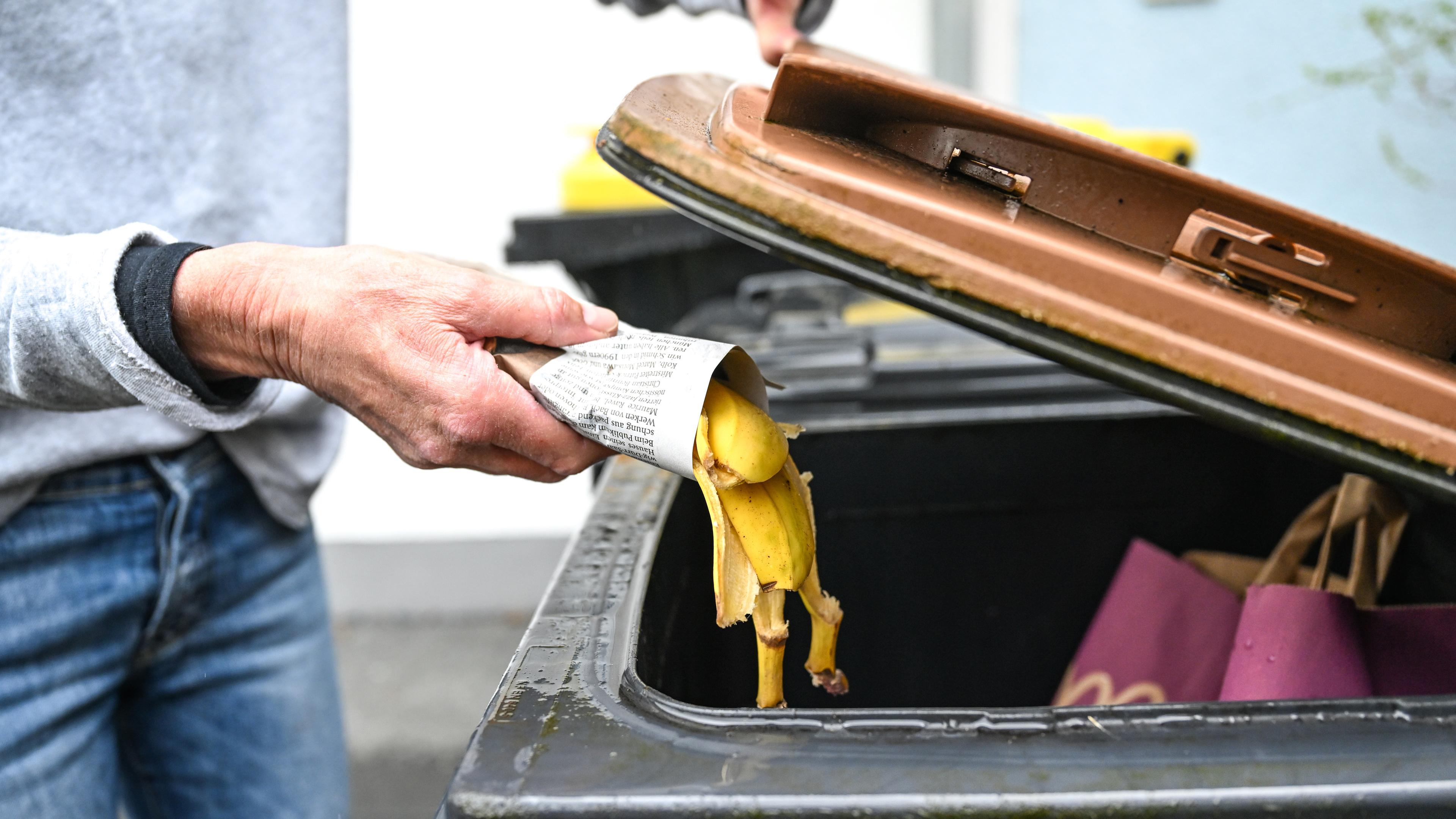 Eine Frau wirft in Zeitungspapier gewickelte Bananenschalen in eine Mülltonne für den Biomüll.