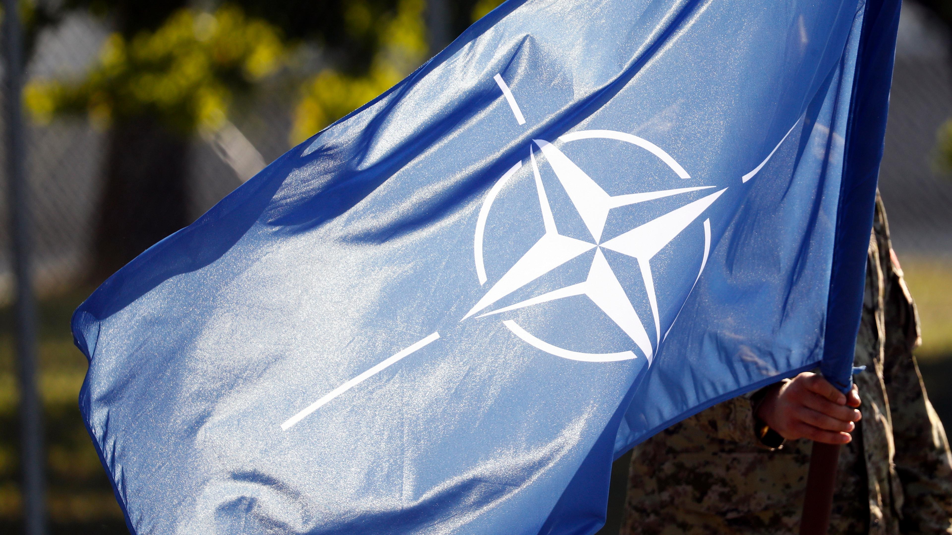 Ein Soldat hält eine Flagge der Nato auf einer Militärbasis in Lettland.