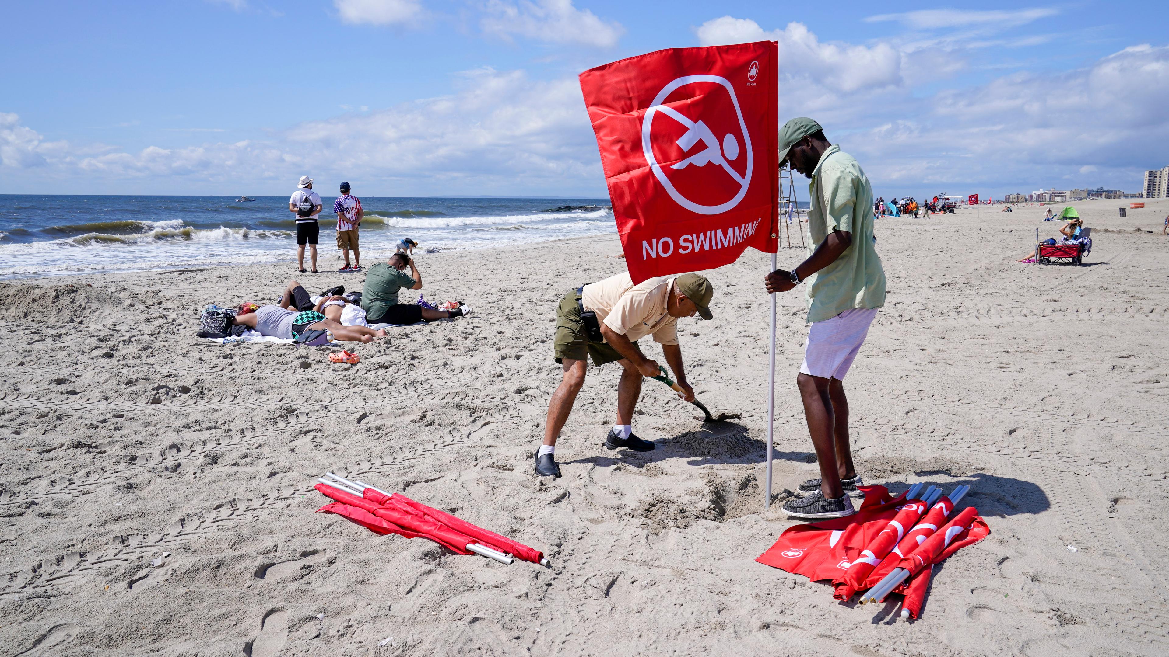 Männer stellen rote Flaggen mit der Aufschrift "No swimming" am Strand auf.