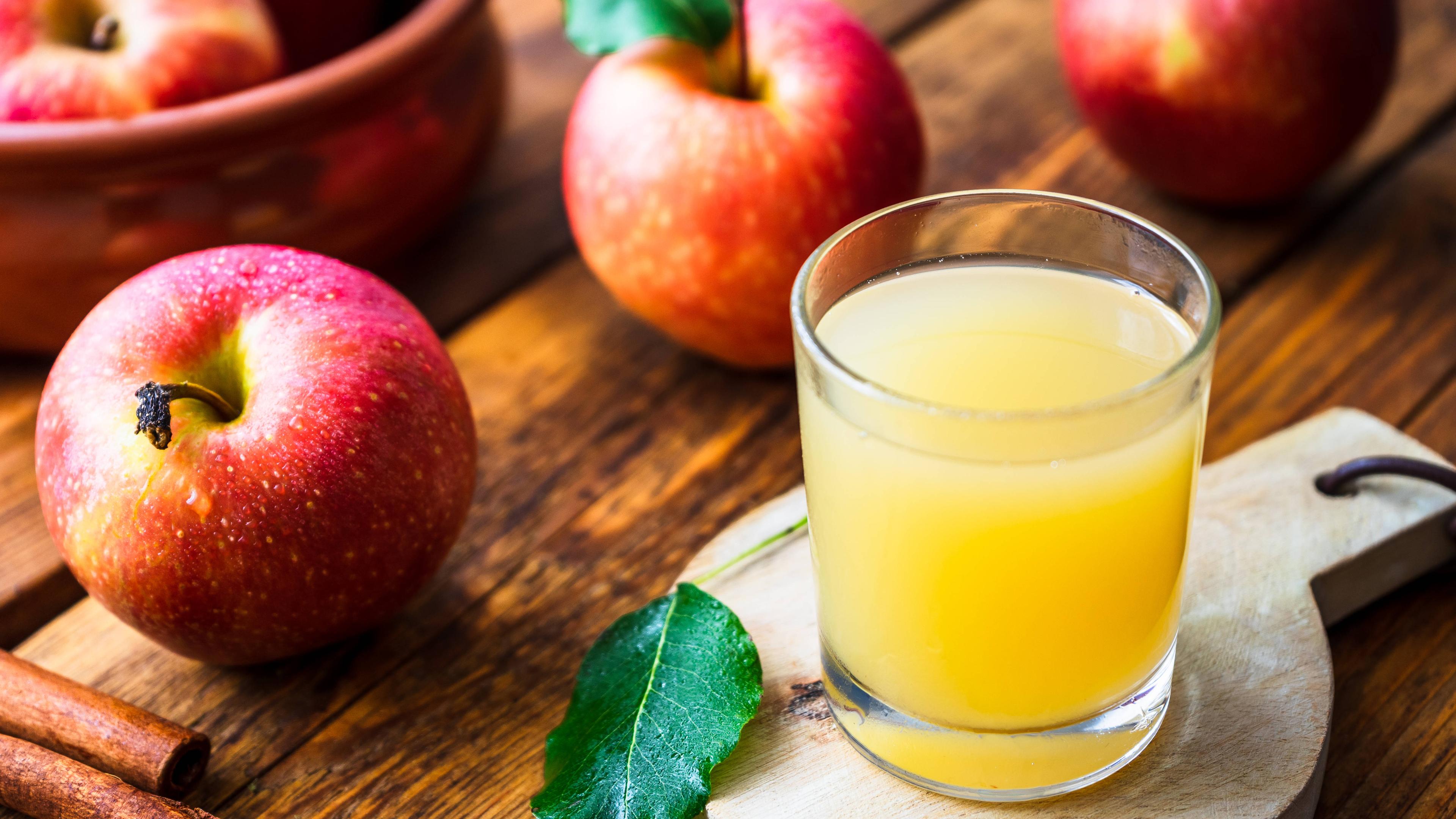 Ein Glas mt naturtrübem Apfelsaft steht af einem Brettchen, drumherum liegen Äpfel.