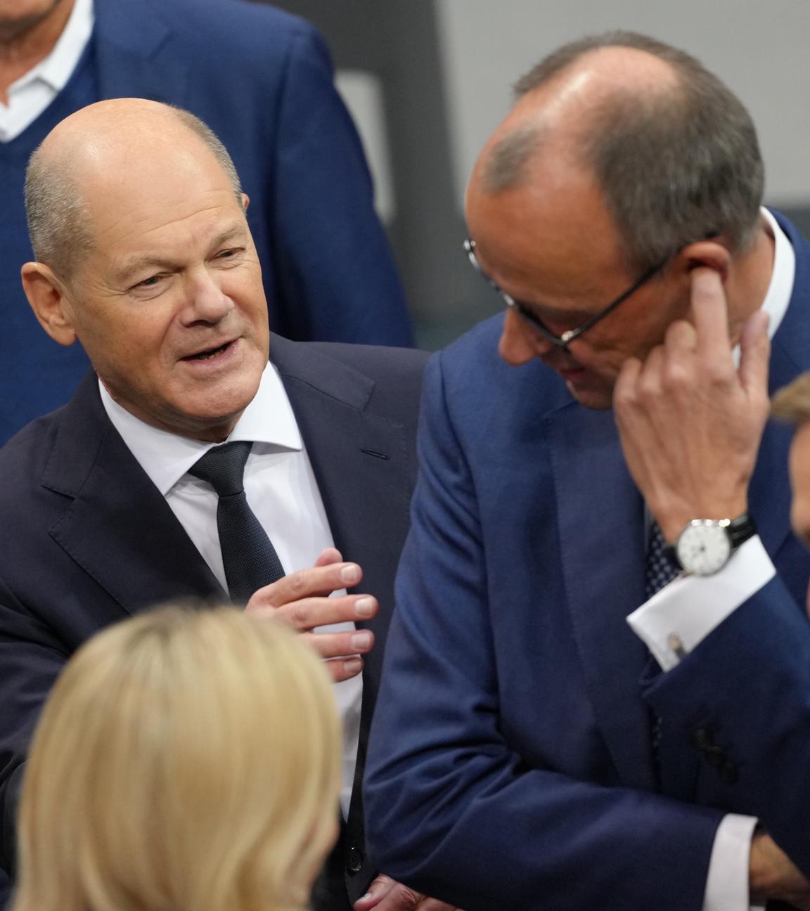 Bundeskanzler Olaf Scholz (SPD, l) spricht im Plenum des Bundestags vor seiner Regierungserklärung mit Friedrich Merz (M)