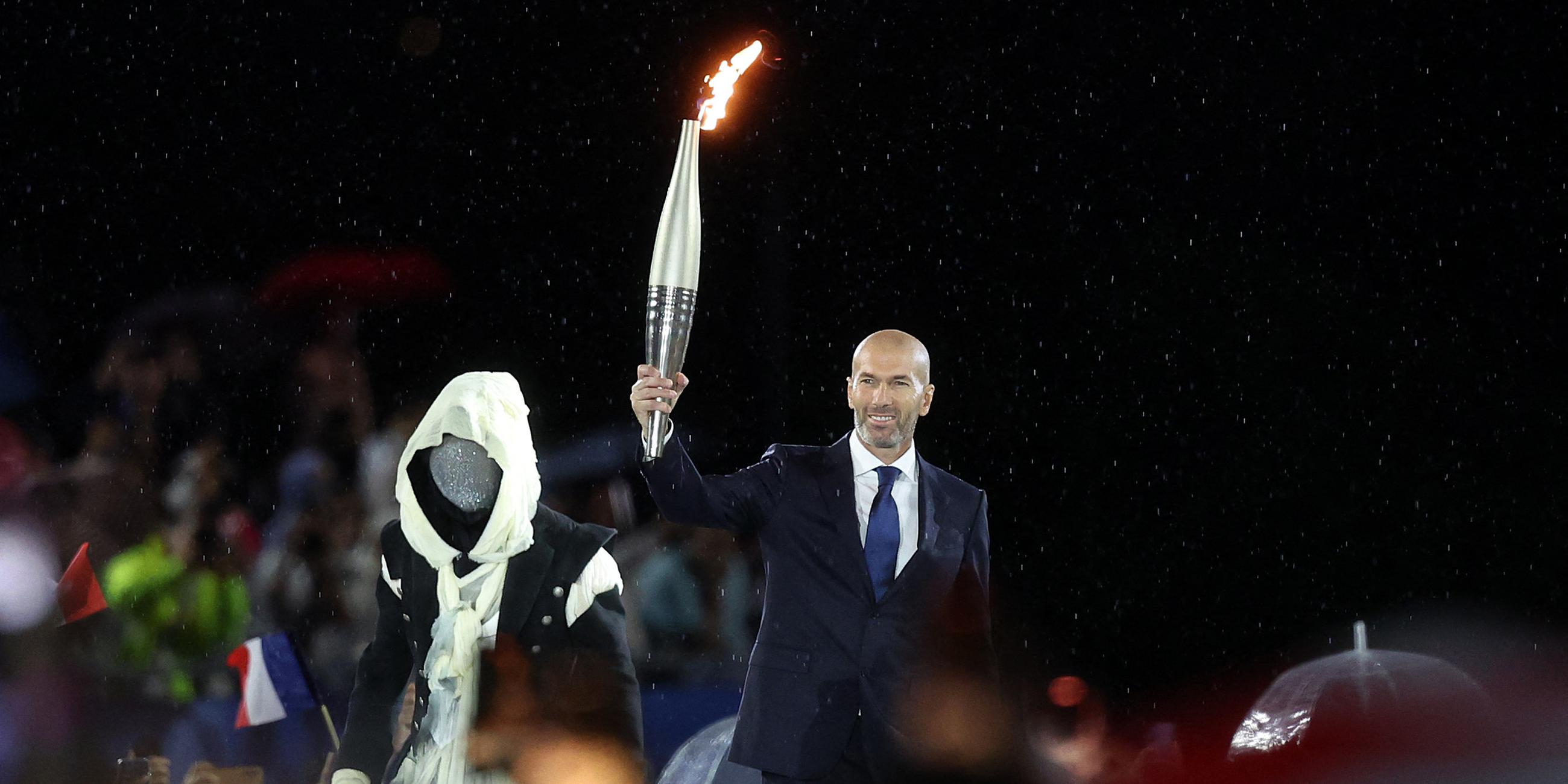 Zinedine Zidane, ehemaliger französischer Fußballspieler und -manager, hält die olympische Fackel