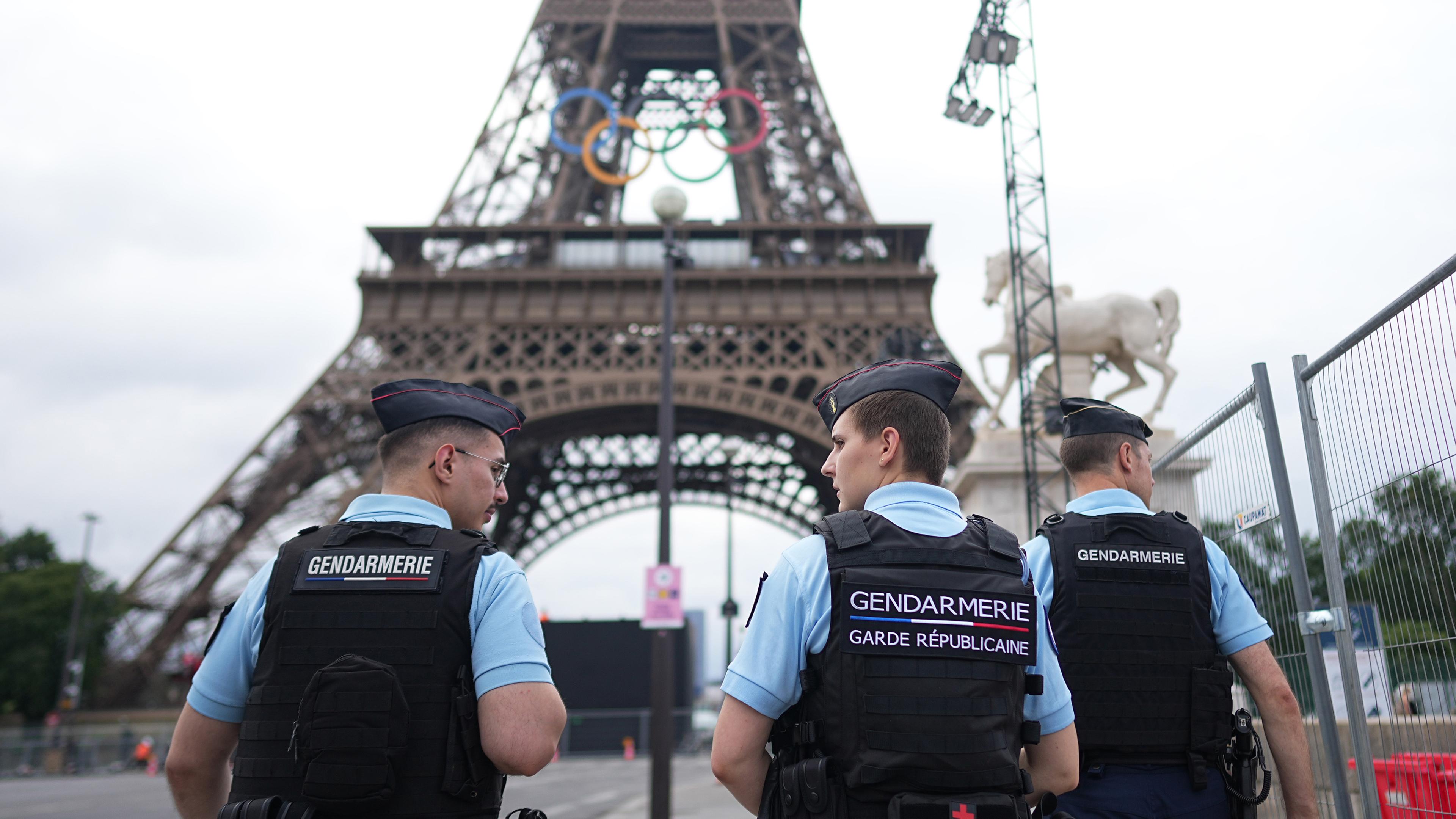 Frankreich, Paris: Vor den Olympischen Sommerspielen, Paris 2024, Polizisten laufen am Eiffelturm entlang.