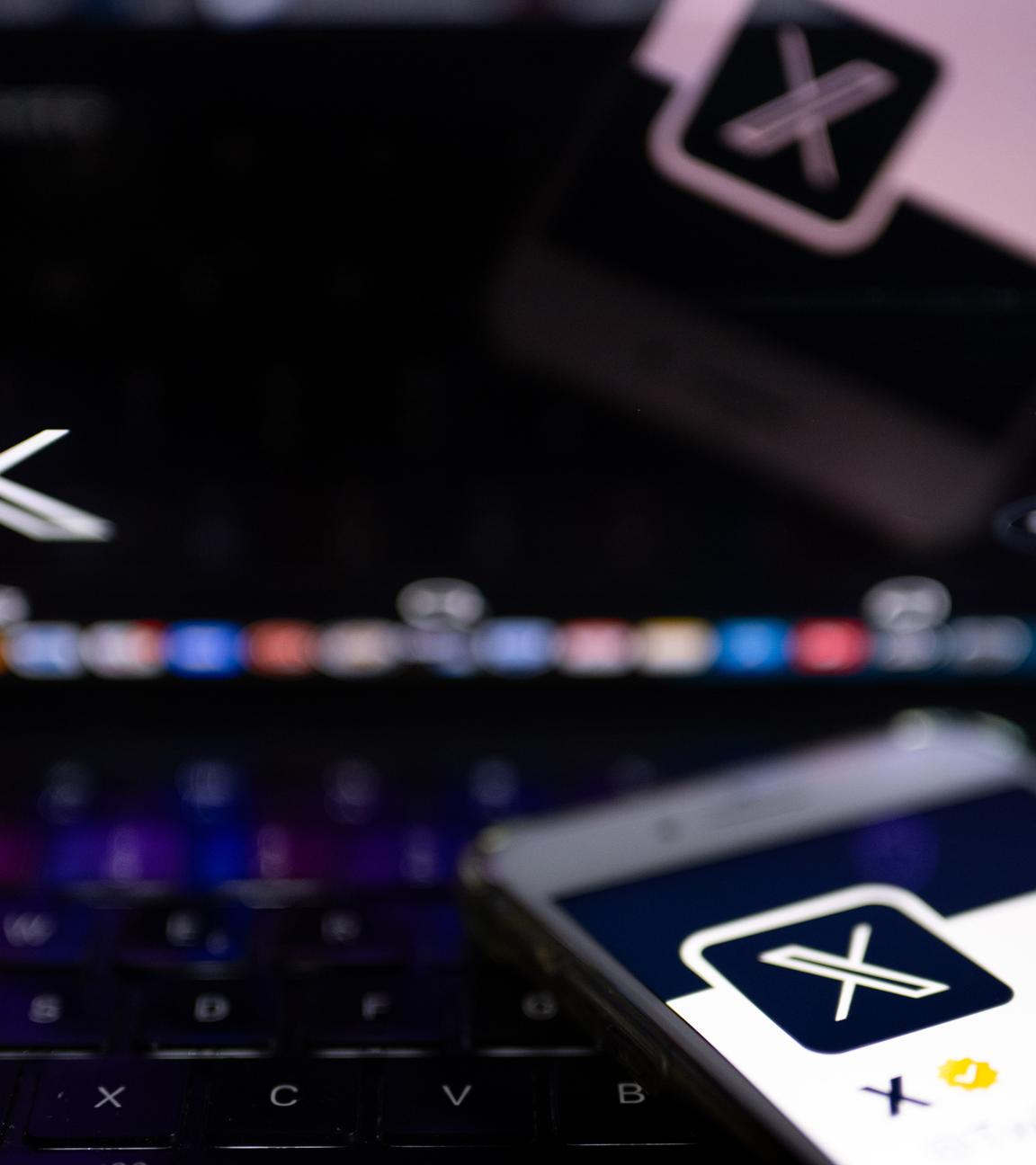 Auf dem offiziellen Profil der Plattform X auf dem Bildschirm eines Smartphones und auf dem Display eines Laptops ist der weiße Buchstabe X auf schwarzem Hintergrund zu sehen. 