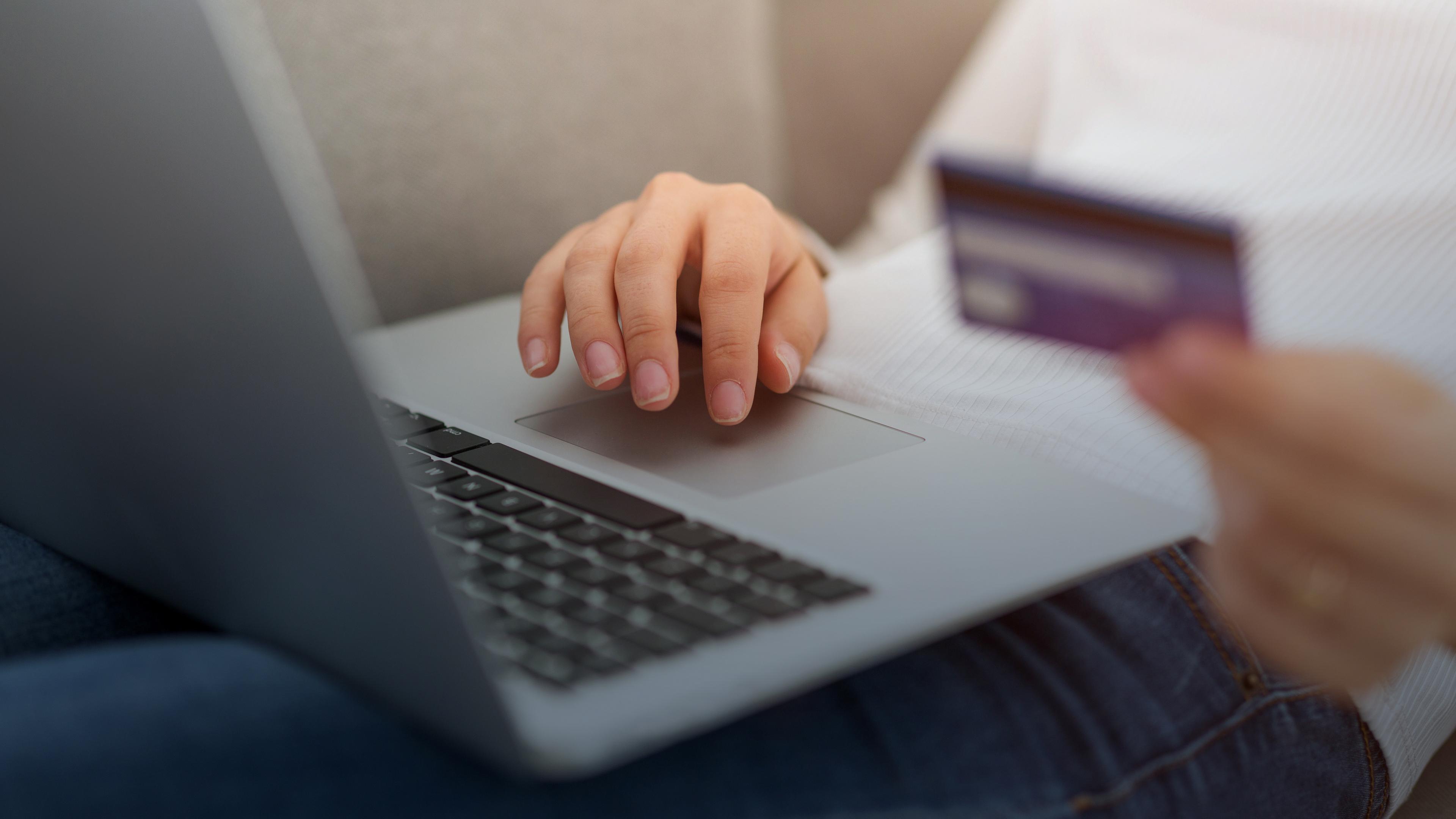 Eine Frau sitzt mit einem Laptop und einer Kreditkarte auf der Couch