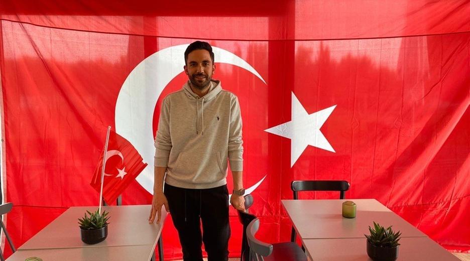 Onur Tuac, Vorstandsmitglied beim Verein Anadolu Türkspor, steht im Vereinsheim vor einer türkischen Fahne.