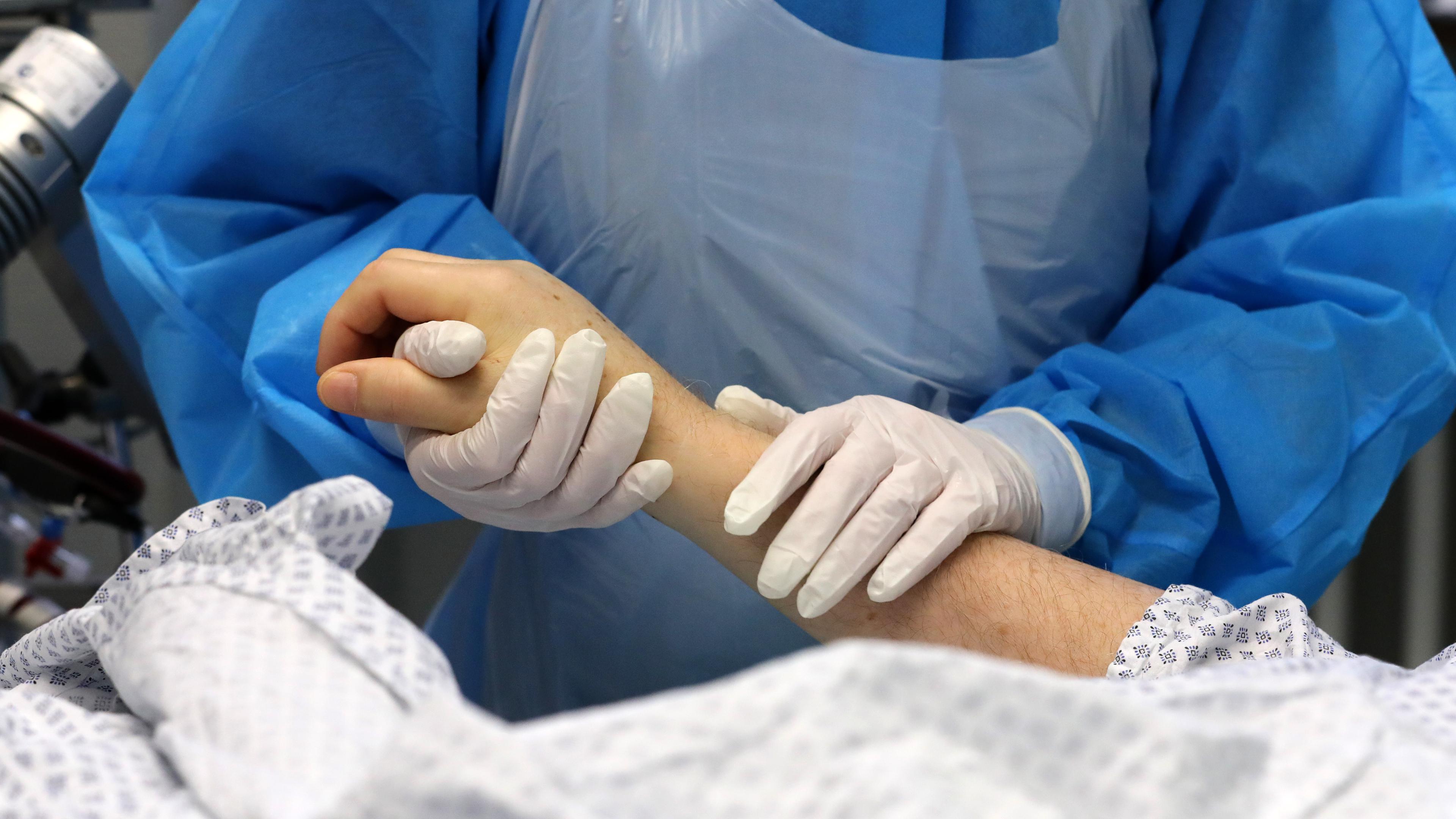 Die Mitarbeiterin einer Intensivstation hält die Hand eines Patienten.