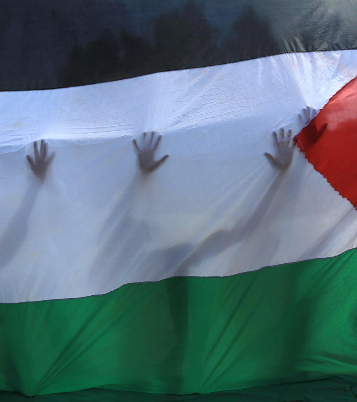  Palästinensische Gebiete, Khan Yunis: Palästinensische Freiwillige stehen hinter einer palästinensischen Fahne, durch die ihre Silhouetten zu erkennen sind.