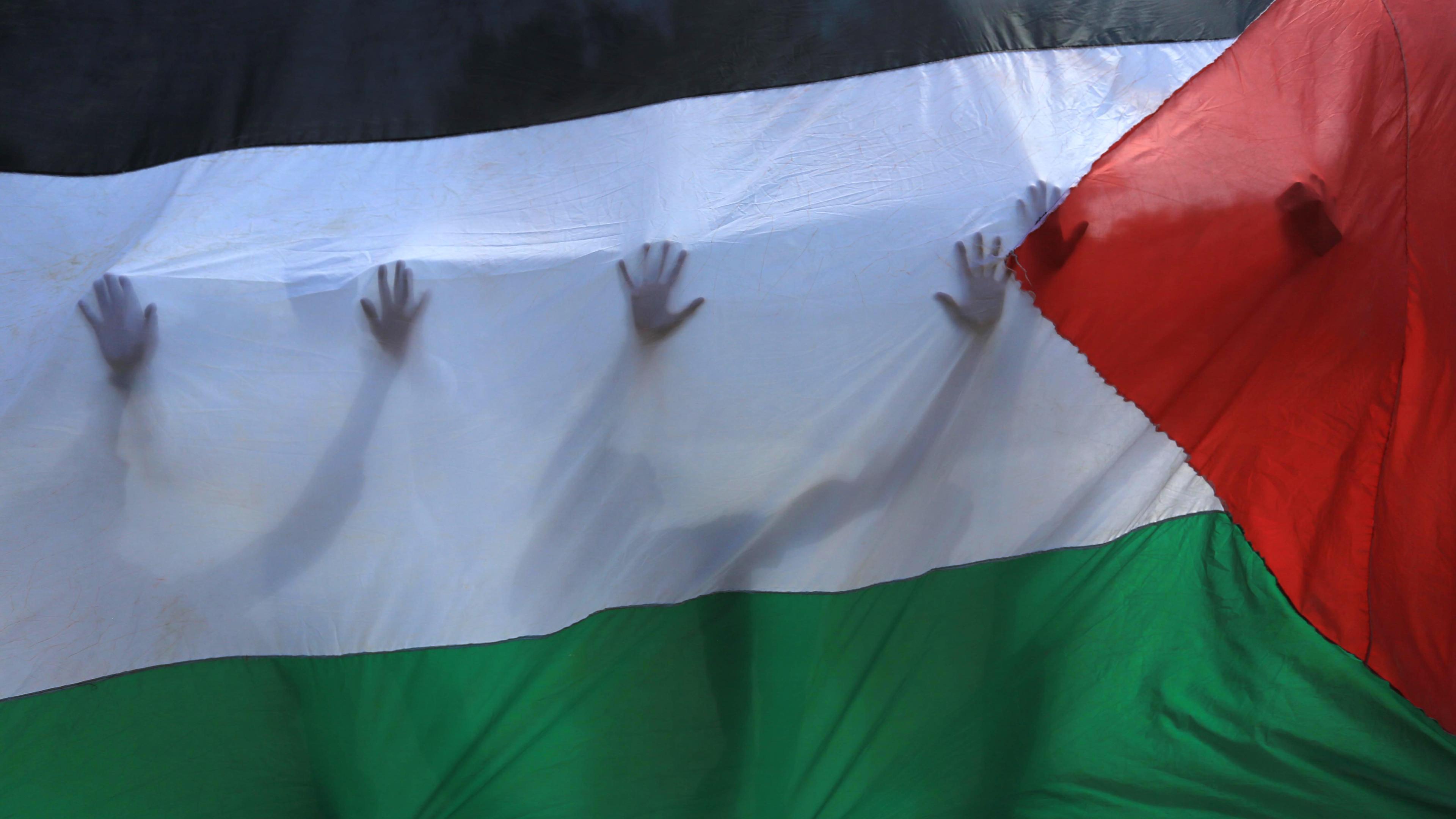  Palästinensische Gebiete, Khan Yunis: Palästinensische Freiwillige stehen hinter einer palästinensischen Fahne, durch die ihre Silhouetten zu erkennen sind.
