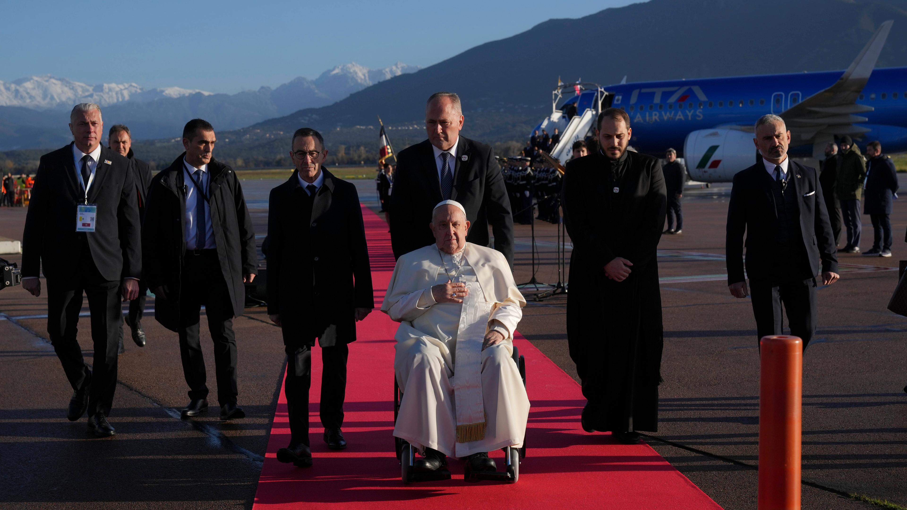 15.12.2024, Frankreich, Ajaccio: Papst Franziskus wird bei seiner Ankunft auf dem internationalen Flughafen von Ajaccio anlässlich seines eintägigen Besuchs auf der französischen Insel Korsika von den örtlichen Behörden begrüßt.