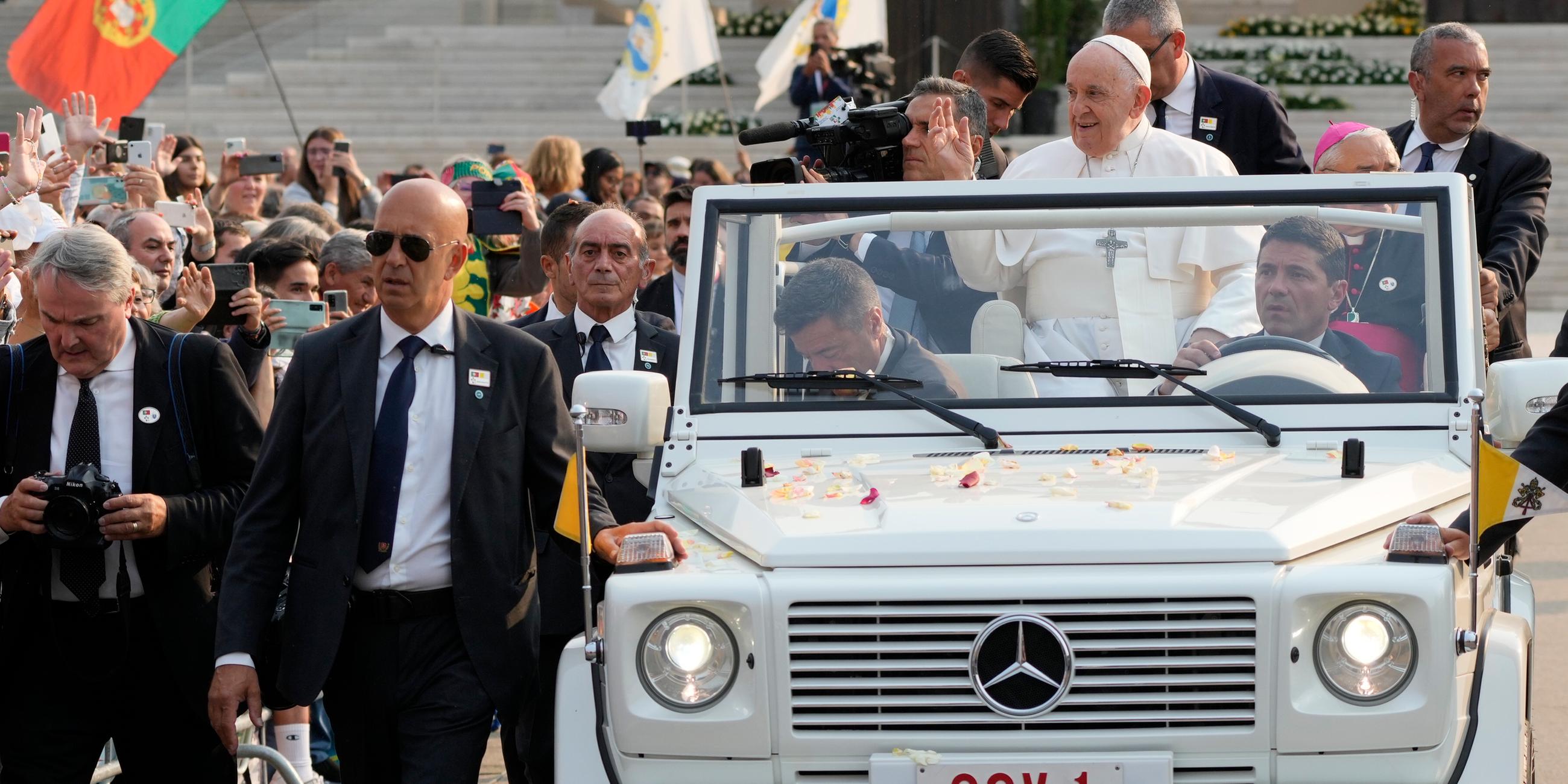 Papst in weißem Auto umgeben von Menschen