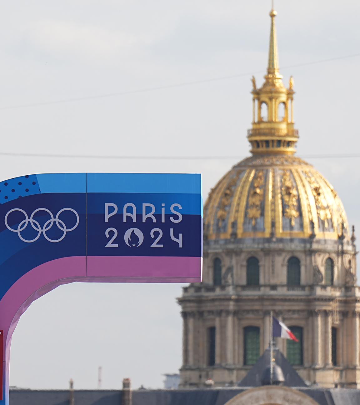 24.07.2024, Frankreich, Paris: Vor den Olympischen Sommerspielen, Olympia Paris 2024, eine Anzeigetafel und die Olympischen Ringe sind vor der Kuppel des Hotel des Invalides zu sehen.
