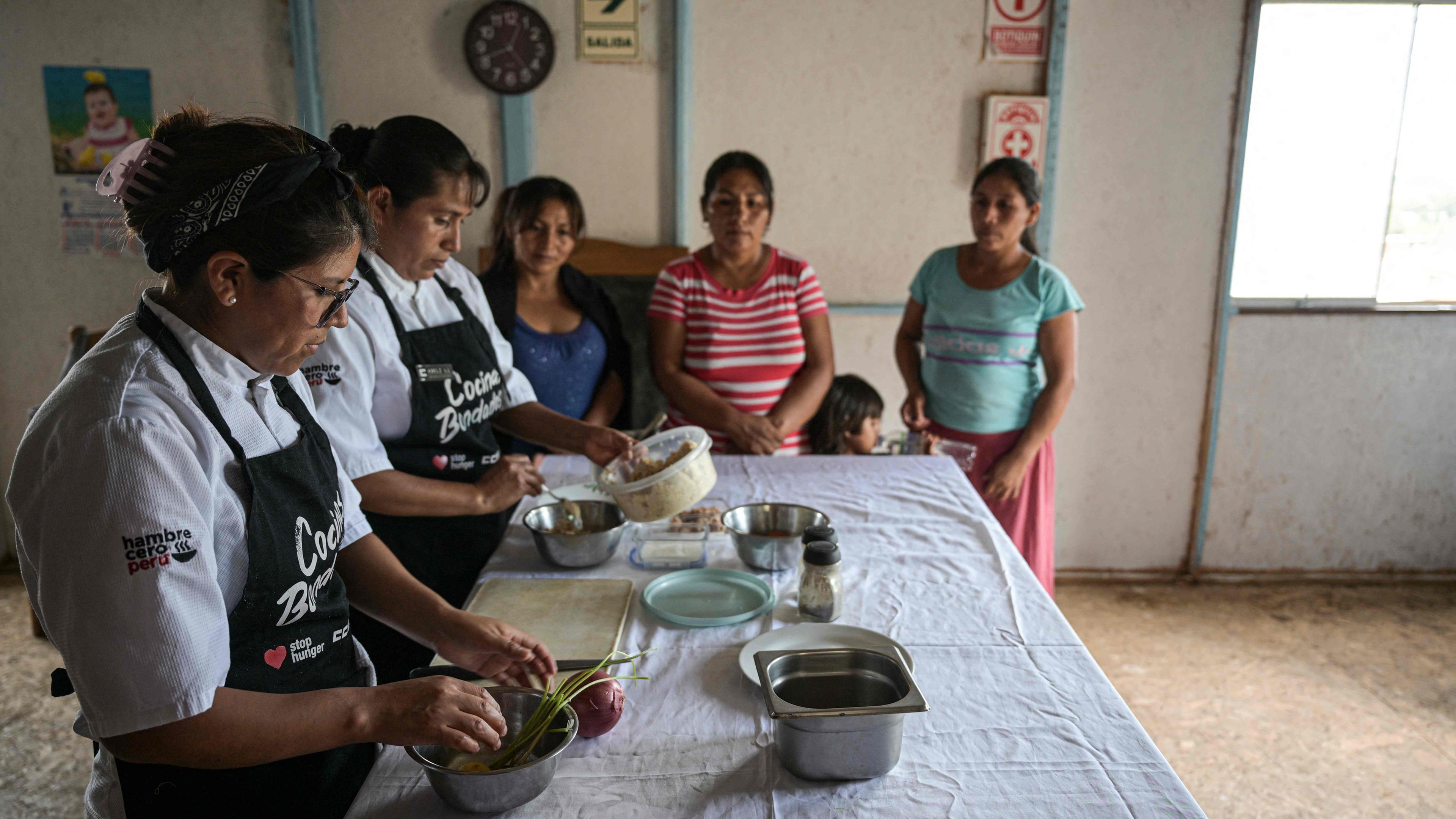 Zwei Köchinnen des Ccori-Projekts kochen vor drei Frauen.