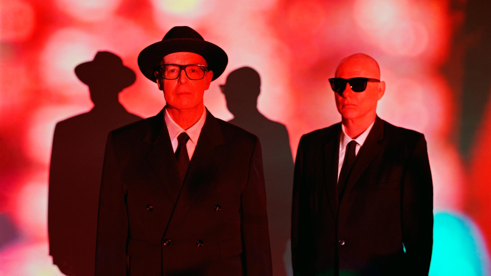 Es sind die Pet Shop Boys zu sehen in rotem Licht und Anzügen.