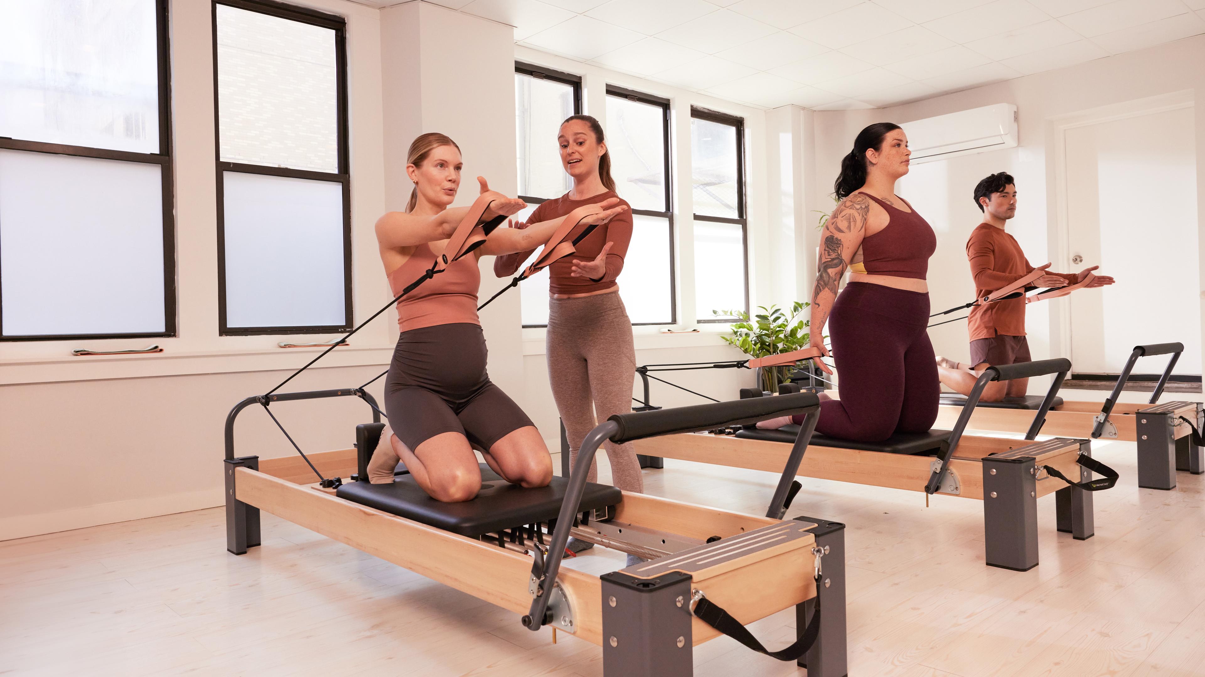 Drei Menschen führen ein Pilatestraining auf einem Reformer durch.